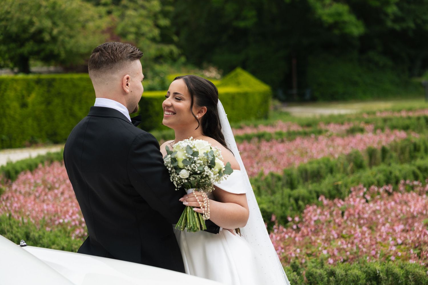 Bride and groom share a romantic moment in a lush garden, bride holding a white bouquet in a elegant wedding dress.