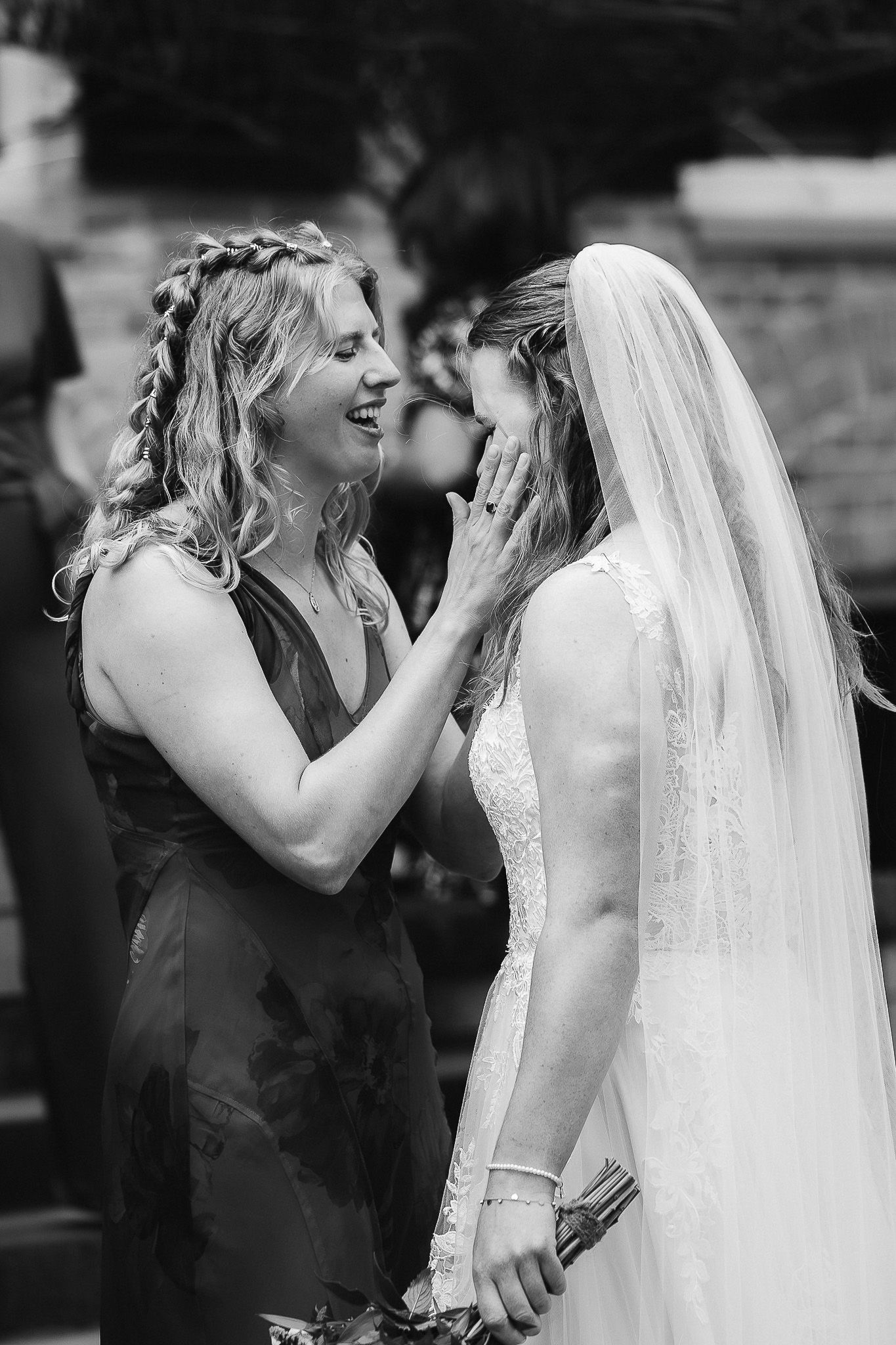 Black and white photo of a bridesmaid tenderly touching a bride's face, sharing an emotional moment at a wedding.