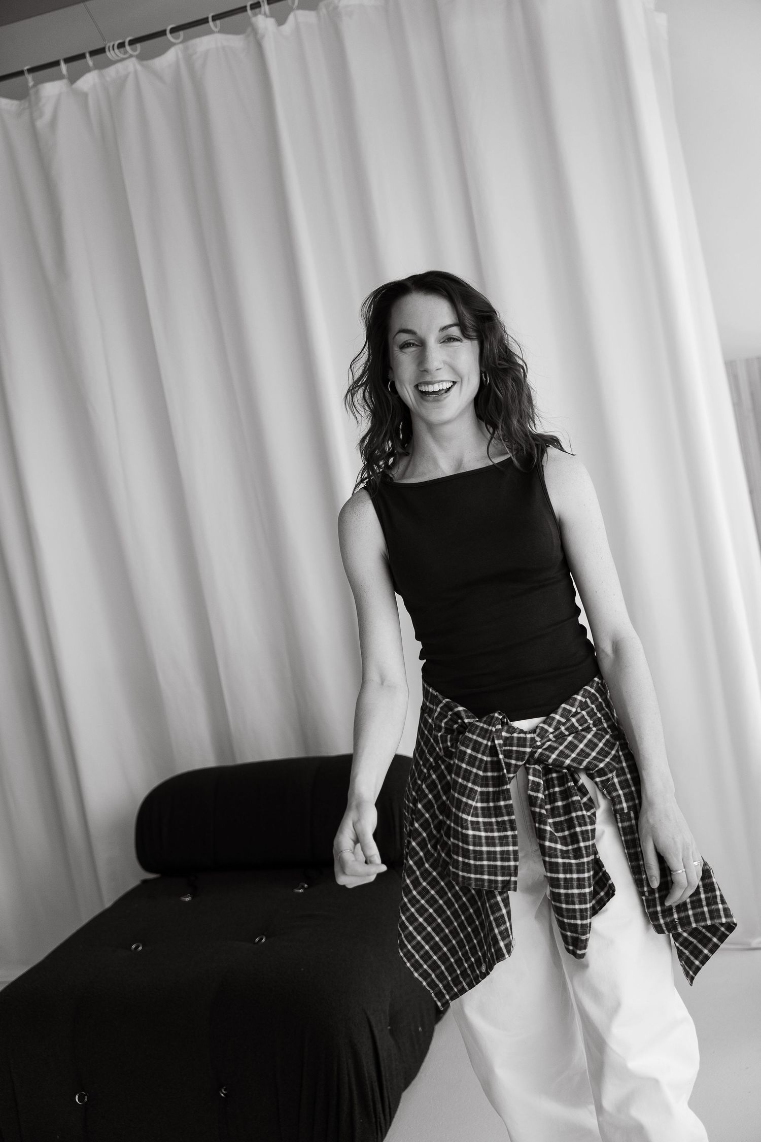 Laughing woman in black tank top with plaid shirt tied around waist, posing in black and white photo.