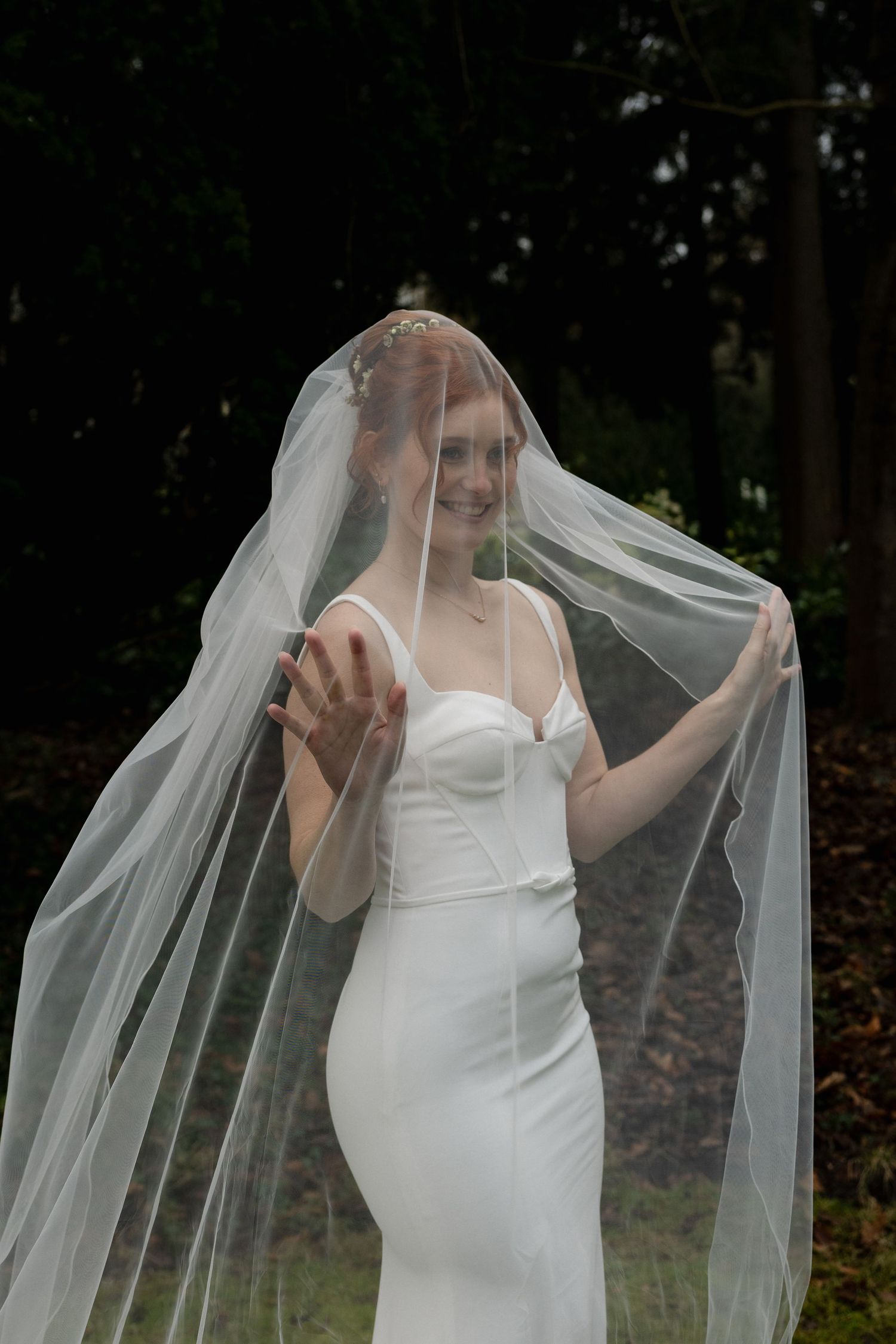 en bruid in een aansluitende witte trouwjurk speelt lachend met haar sluier in het bos; ongedwongen trouwfotografie door atelier ROSA