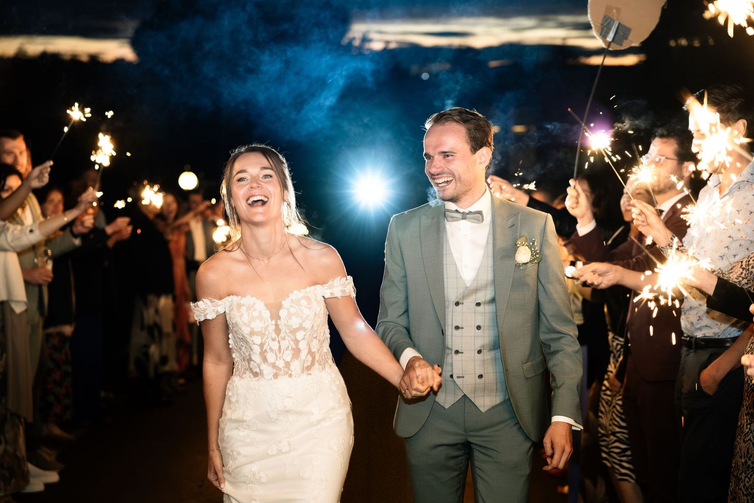 Bride and groom walk through sparkler tunnel at night wedding celebration.