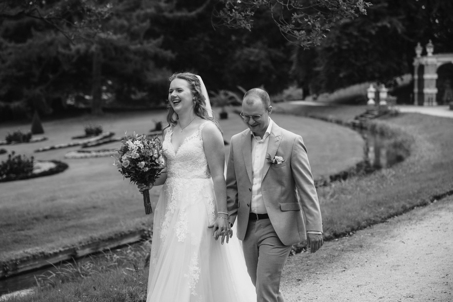 Tijdloze zwart-wit trouwfoto van een lachend bruidspaar in de kasteeltuin van Kasteel Rosendael in Rozendaal