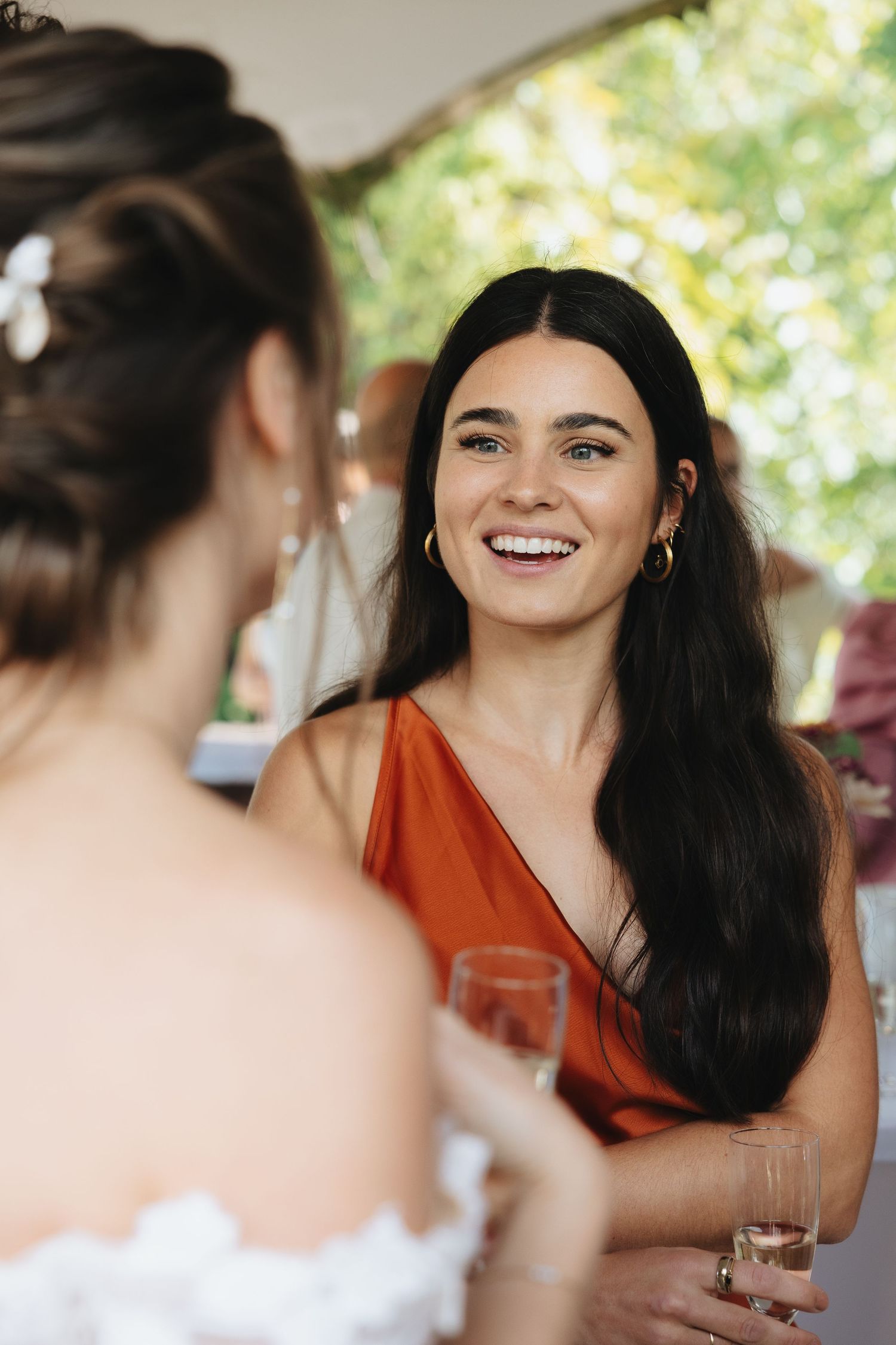 A smiling woman in an orange dress holds a champagne glass at a wedding reception.