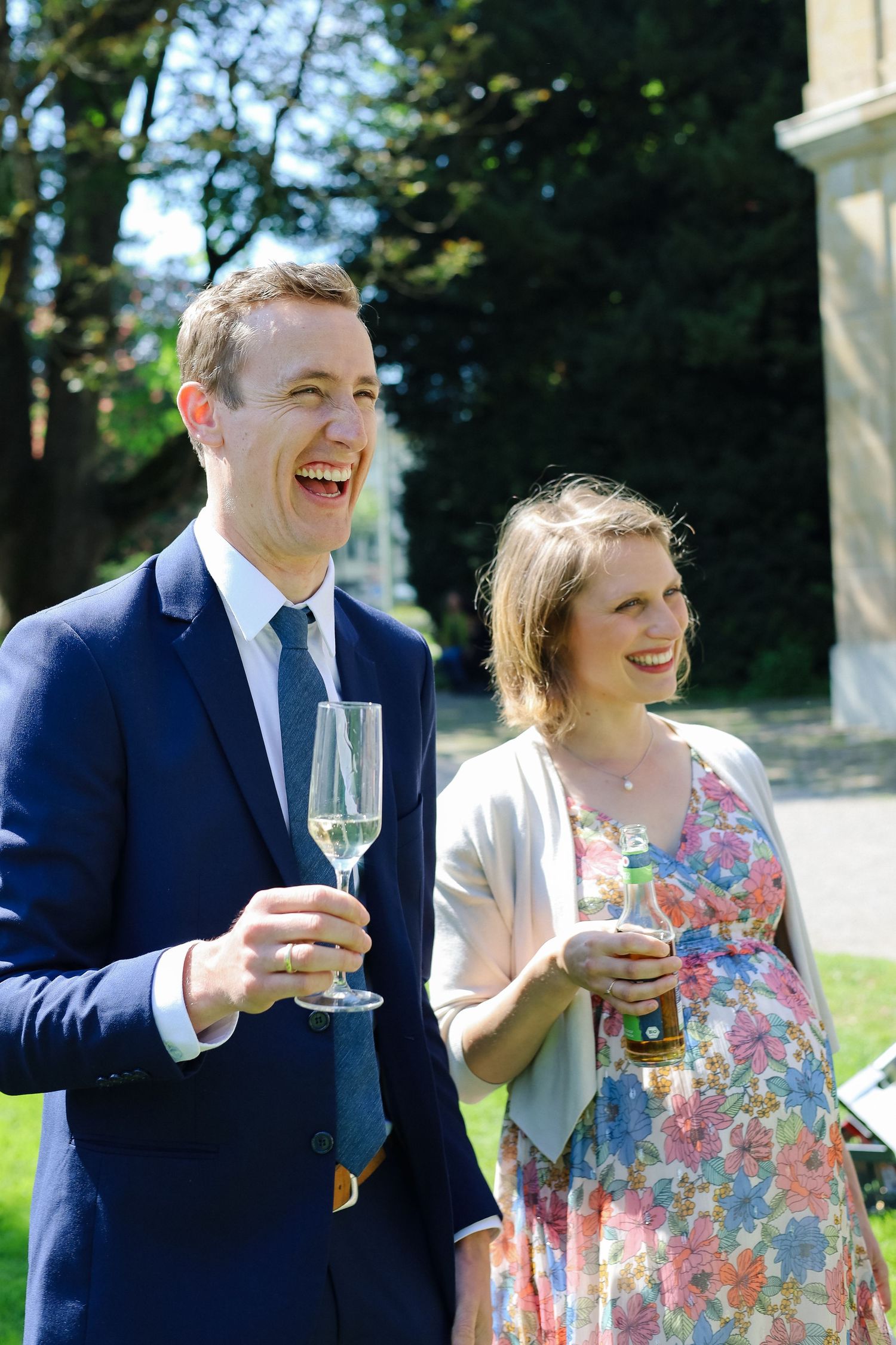 Gasten staan lachend buiten in de zon met champagne tijdens een zomerbruiloft in het buitenland