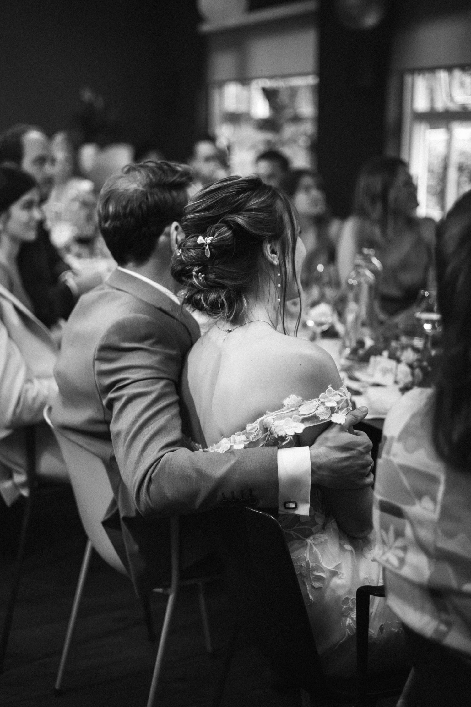 Een tijdloze zwart-wit foto van een intiem moment van een bruidspaar tijdens het diner van hun bruiloft, de man slaat een arm de vrouw