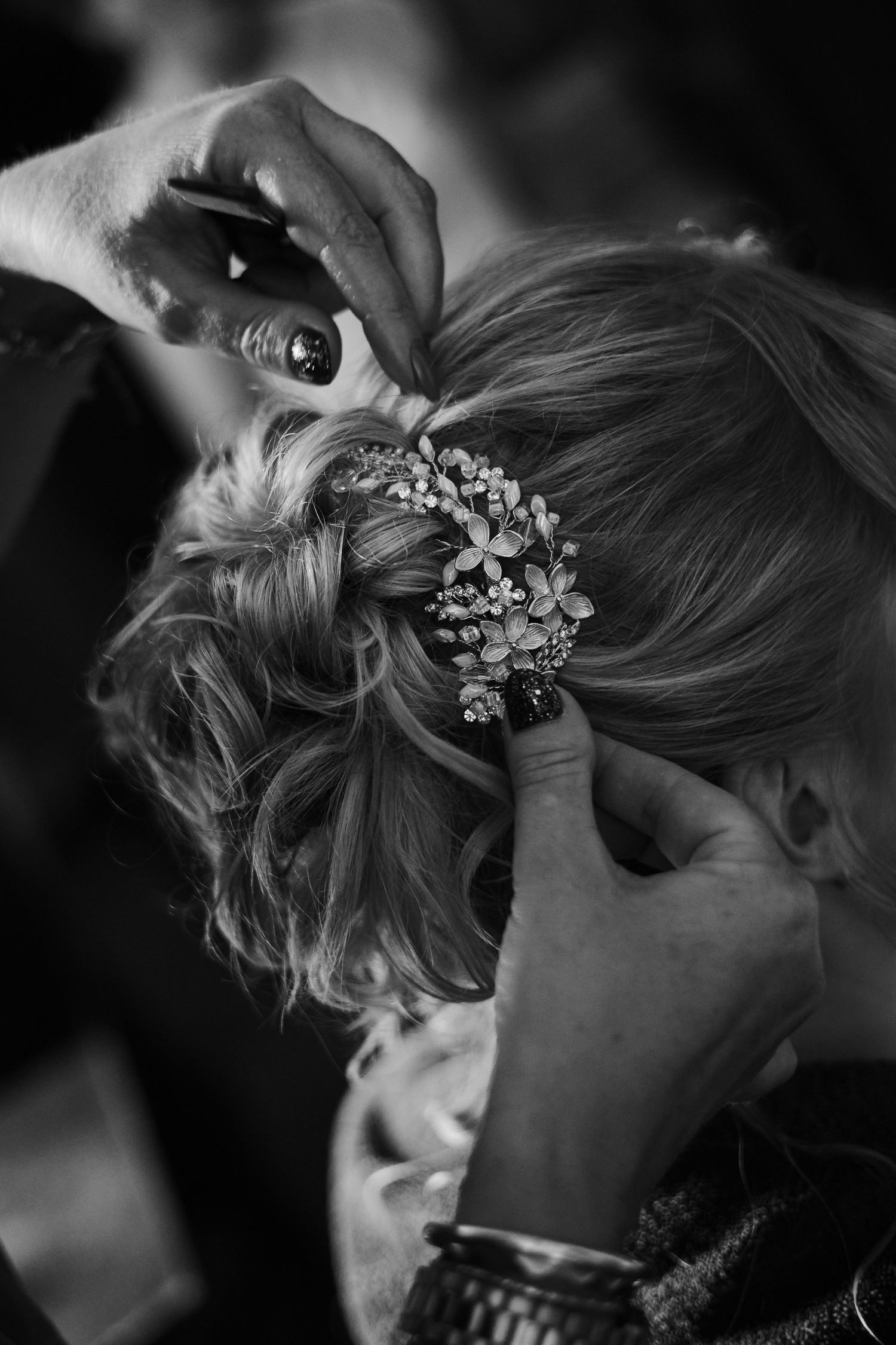 Black and white photo of hands styling a bride's updo with floral hair accessories.