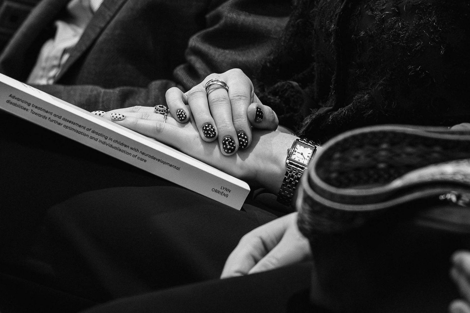 Close-up black and white photo of hands with nail art and a watch resting on an open book.
