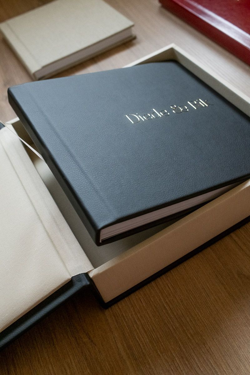 Dark gray hardcover photo book in a white gift box on a wooden table with other books in the background.