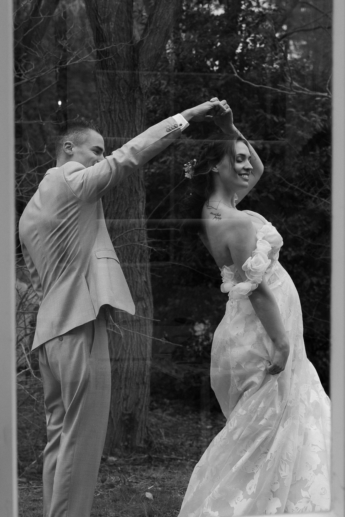 Black and white photo of a groom spinning his bride in a wedding dance outdoors among trees.