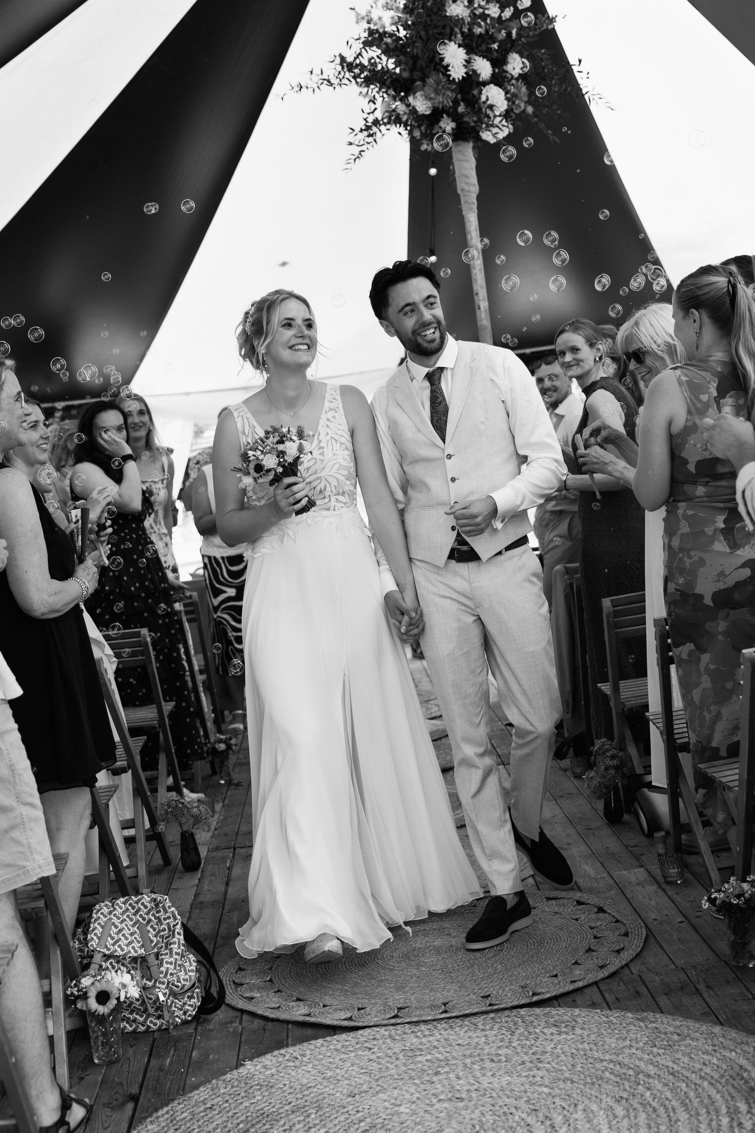 Black and white photo of a joyful bride and groom walking down the aisle after their outdoor wedding ceremony.