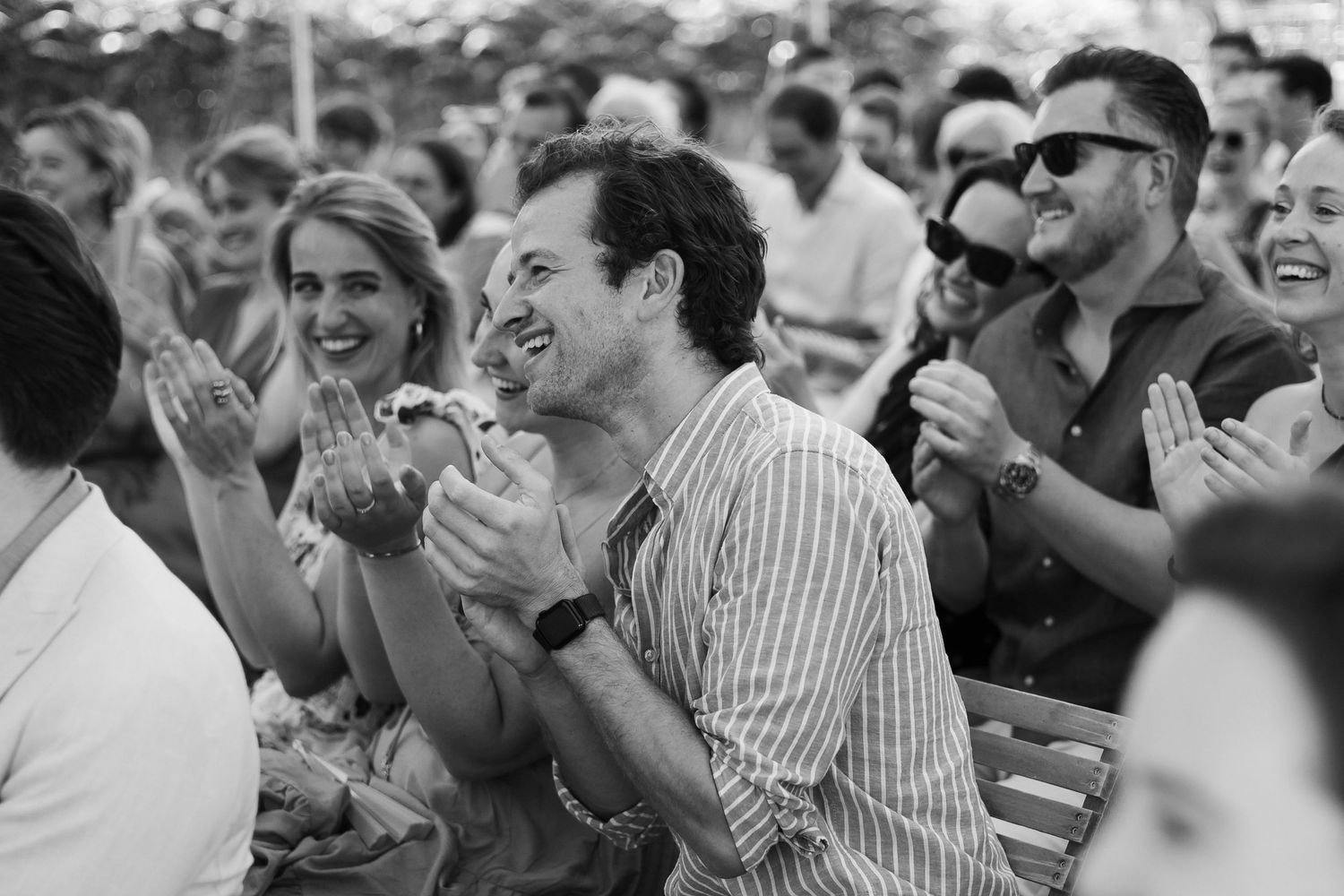 Black and white photo of smiling audience members clapping at an outdoor event.