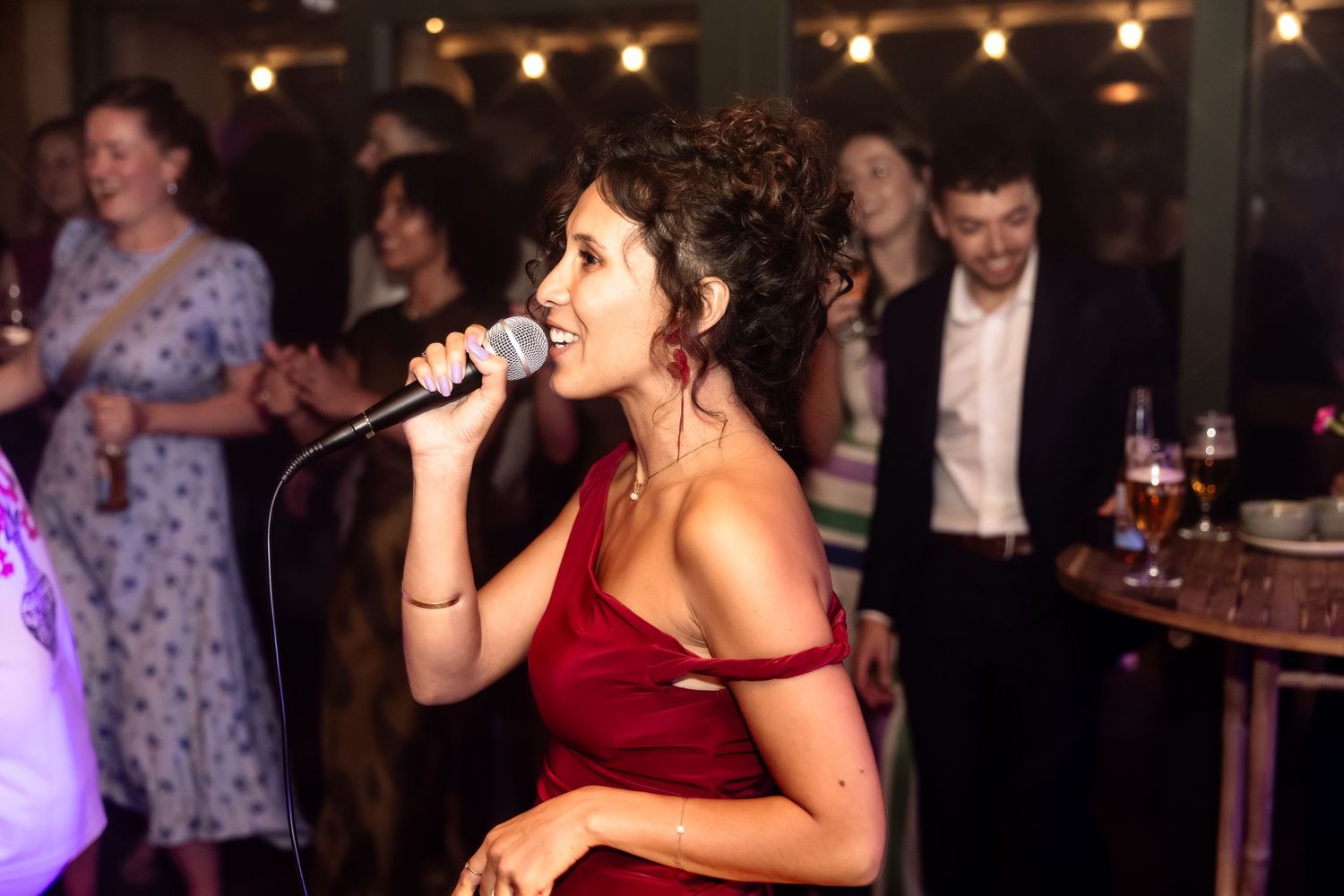 Woman in red dress singing into microphone at lively indoor event.