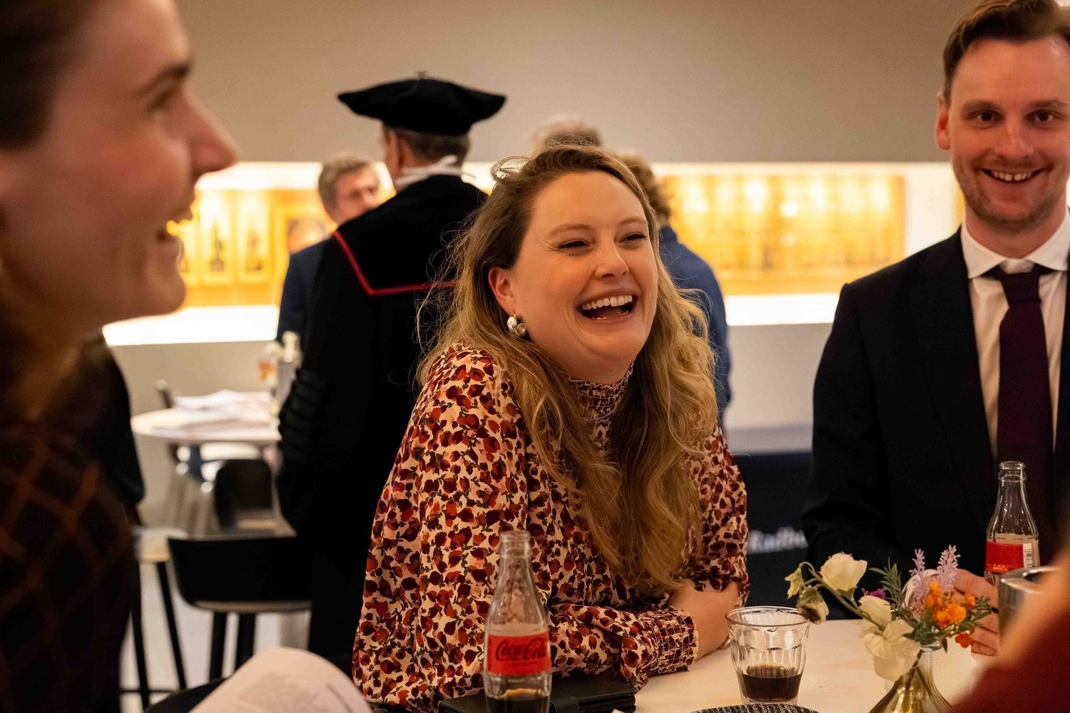 Woman in leopard print top laughing joyfully at a social gathering or dinner event.