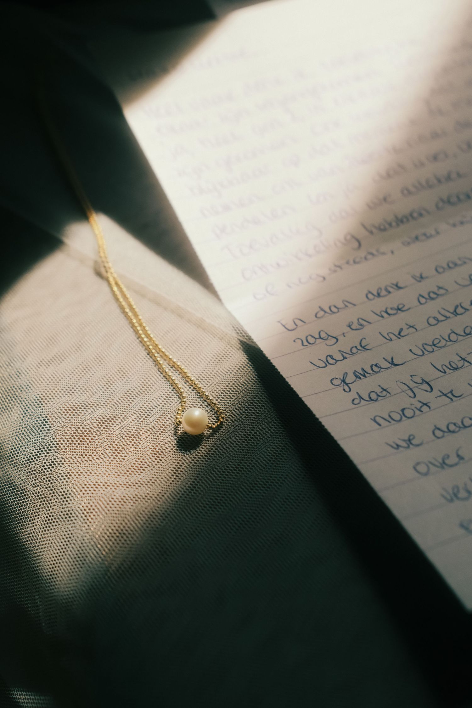 Gold chain pearl necklace resting on handwritten letter journal page in warm sunlight shadow.