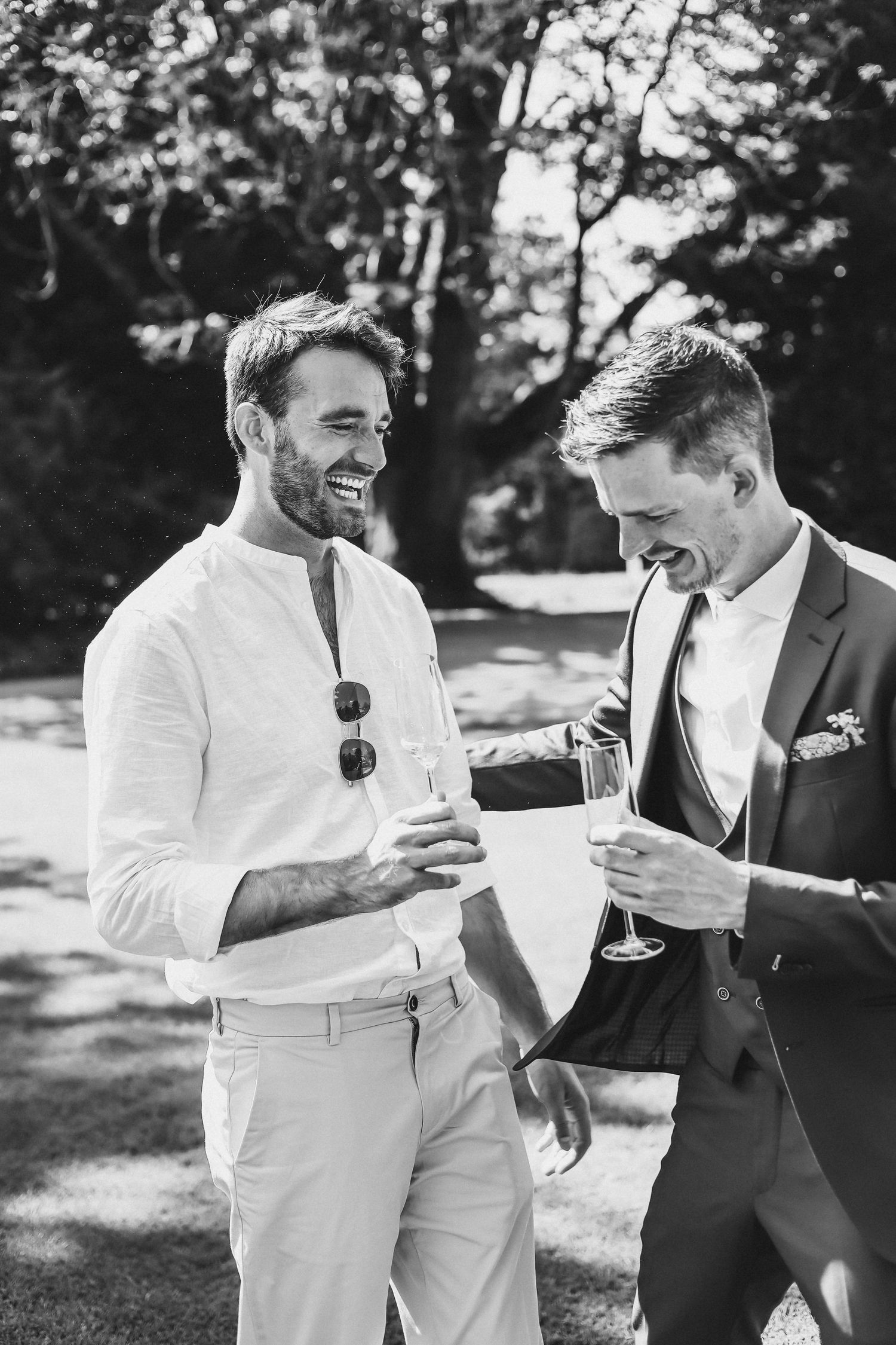 Proosten op de vriendschap: bruidegom en zijn beste vriend lachen samen met een drankje in de hand tijdens bruiloft in het buitenland