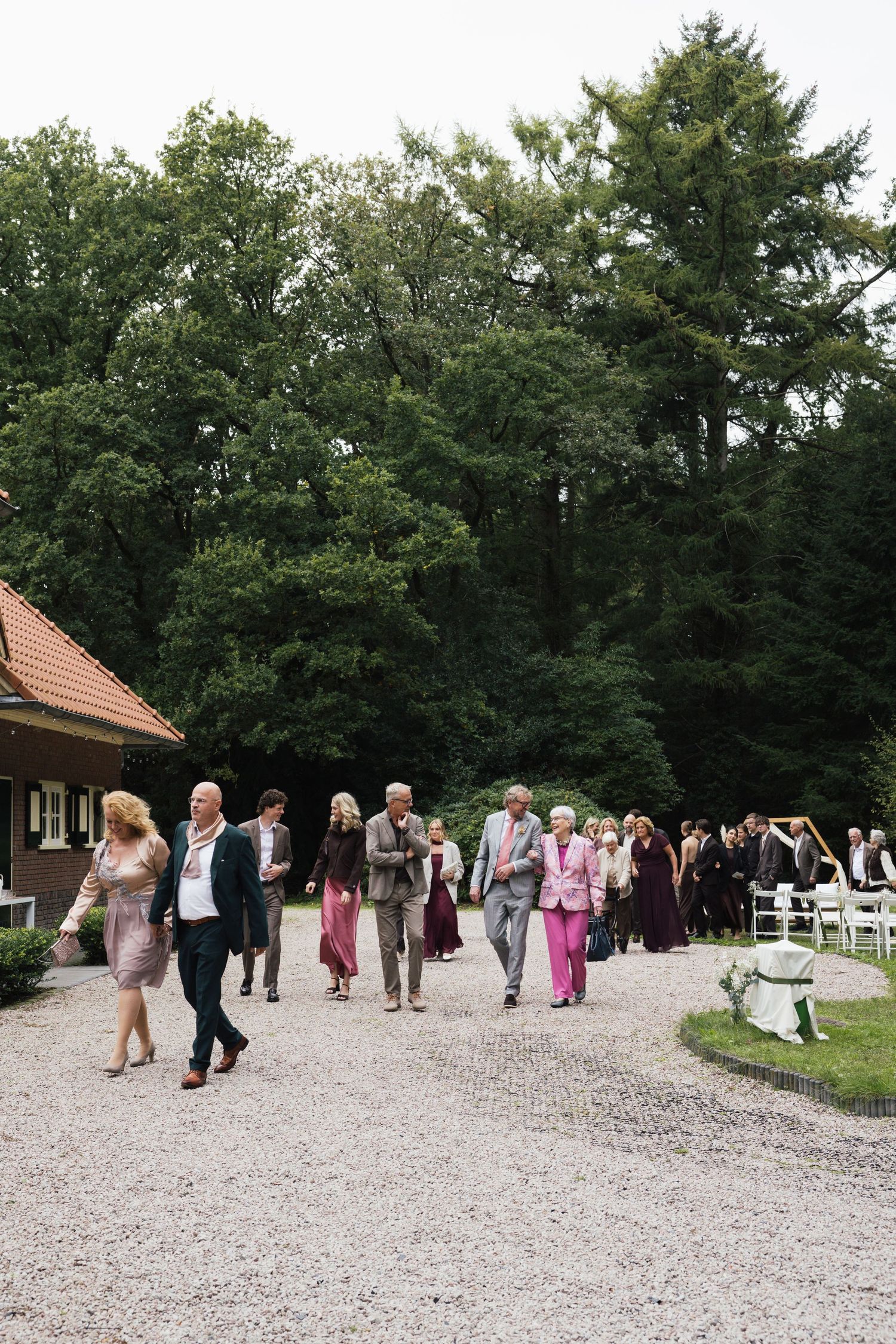 Wedding guests walking along a gravel path surrounded by lush green trees at an outdoor venue.