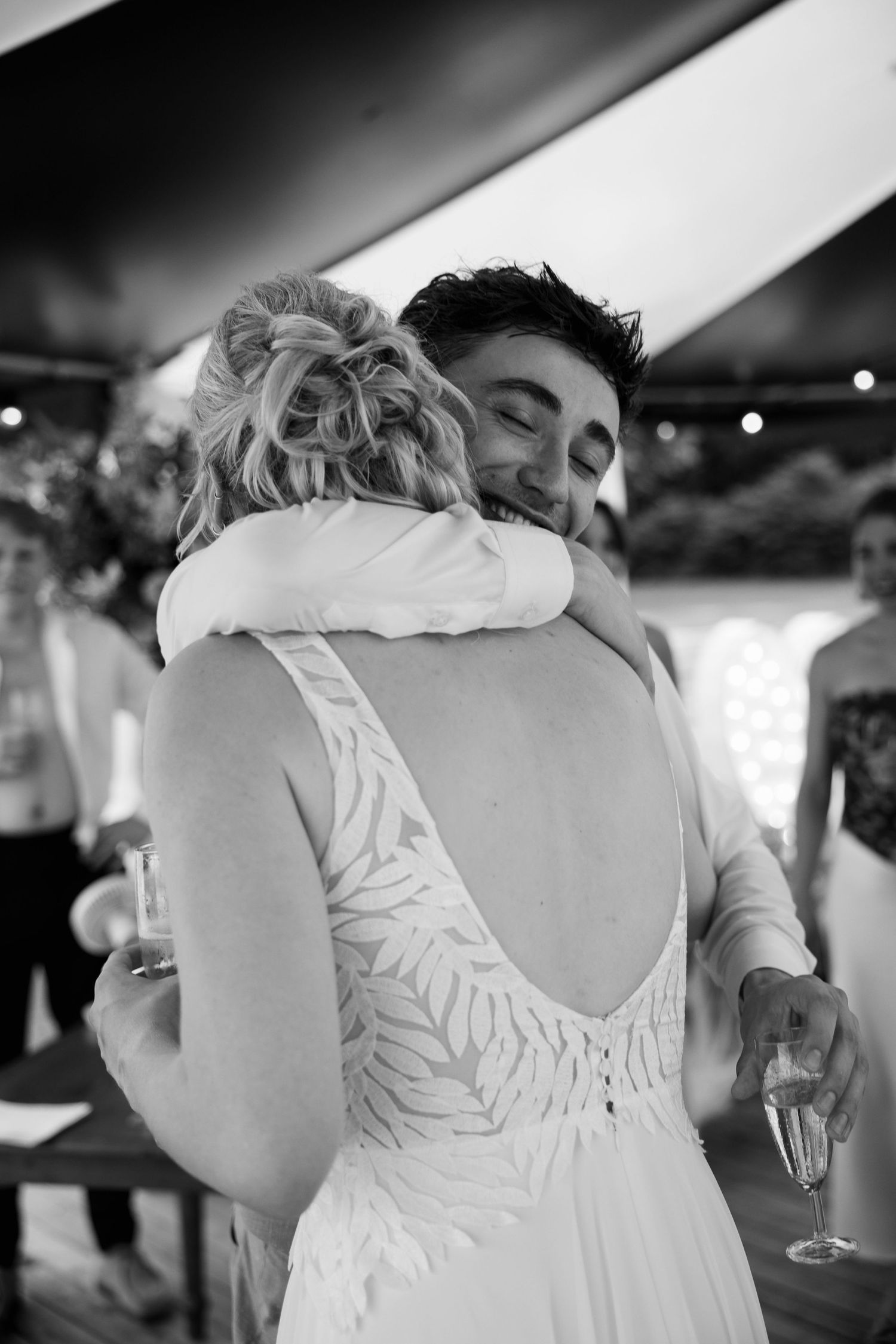 Black and white photo of a bride and groom sharing a joyful embrace, holding champagne glasses at their wedding reception.
