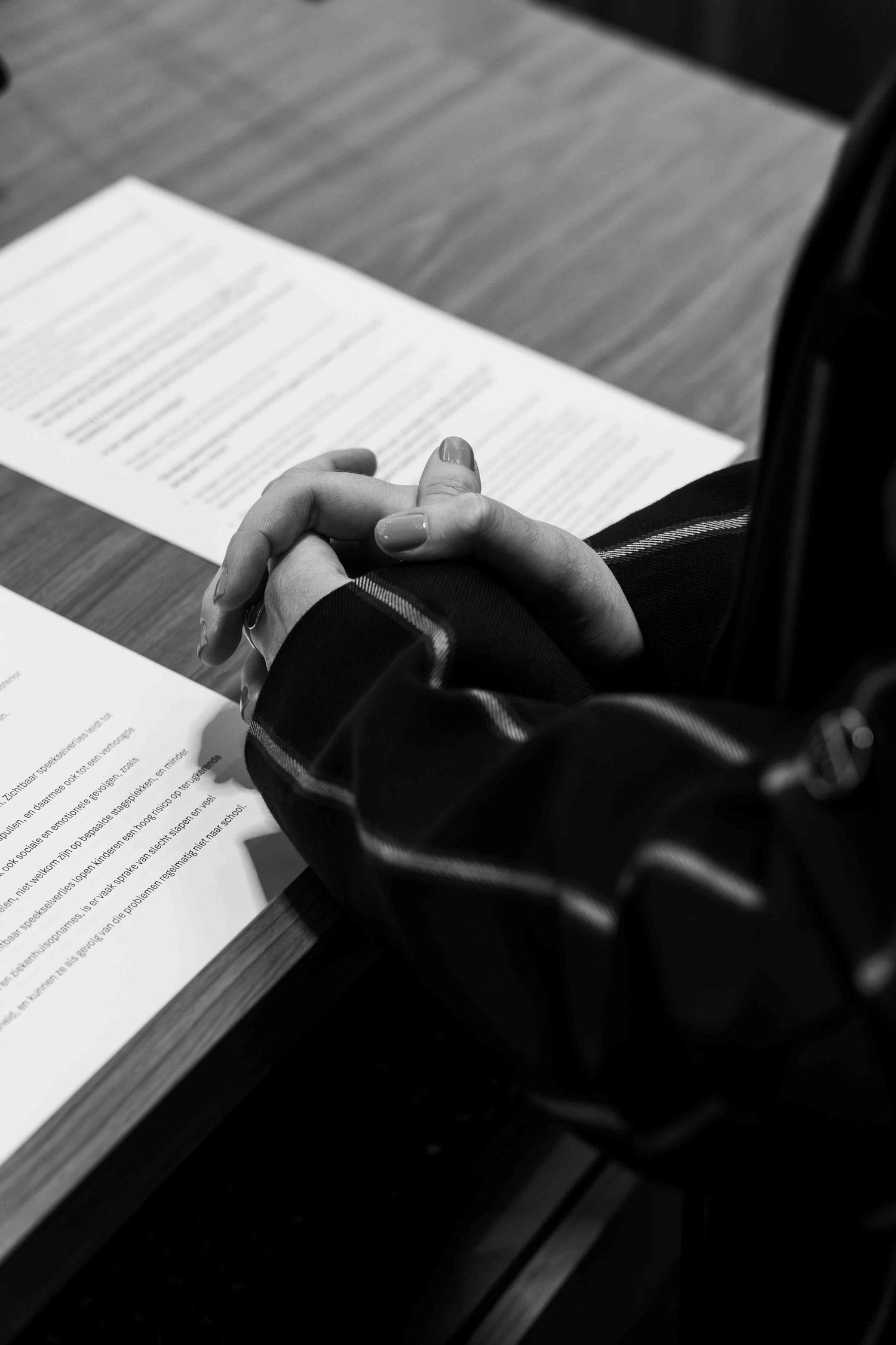 Black and white photo of clasped hands resting on documents at a wooden desk.
