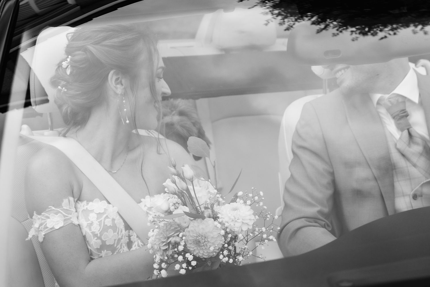 Tijdloos zwart-wit portret van een bruidspaar in de trouwauto; een intiem moment van rust en verbinding tussen de bruid en bruidegom
