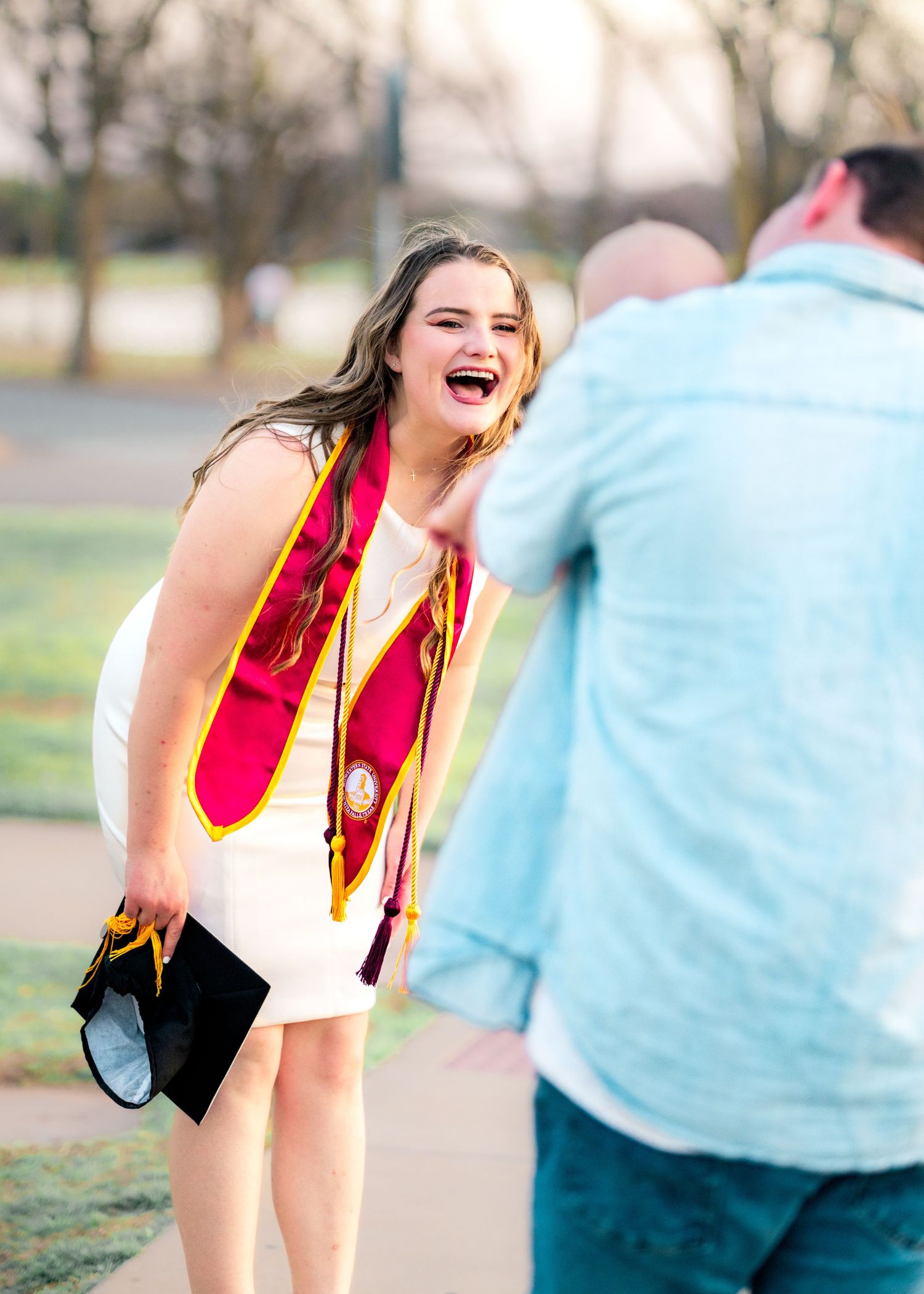 A graduate in red and black regalia shares joyful moments during a photo session.