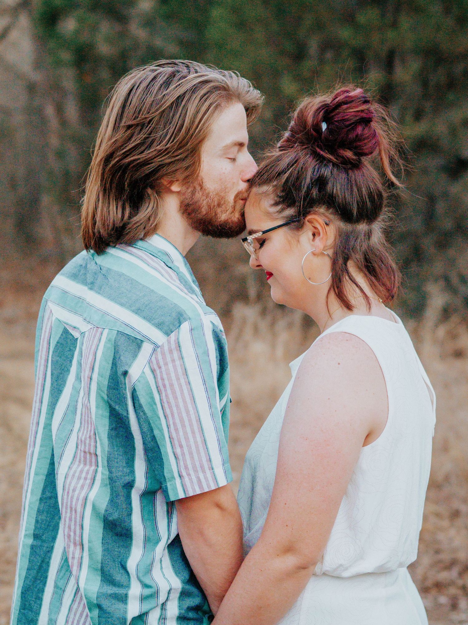 Couple in casual attire sharing tender moment outdoors in natural setting.
