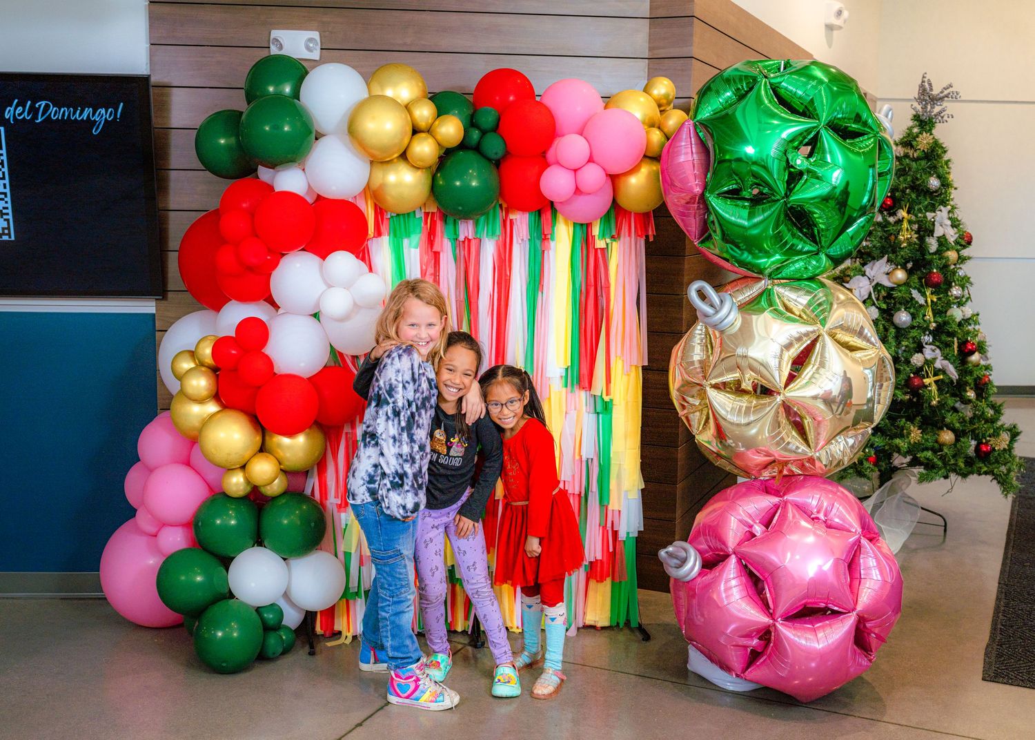 Holiday party setup with elaborate balloon garlands in green, red, and gold against a decorated backdrop.