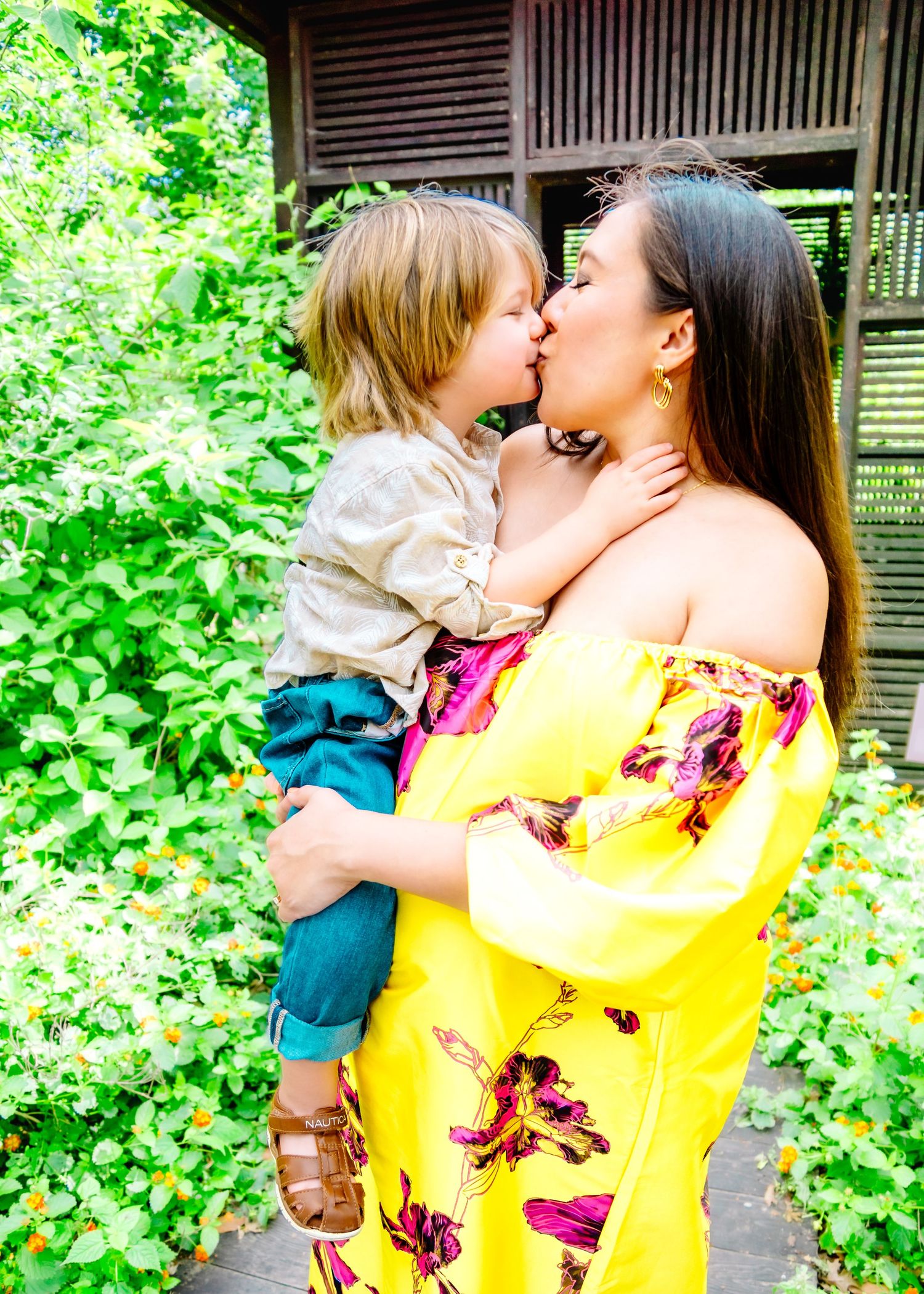 Loving family moment captured in garden setting with rustic wooden structure.