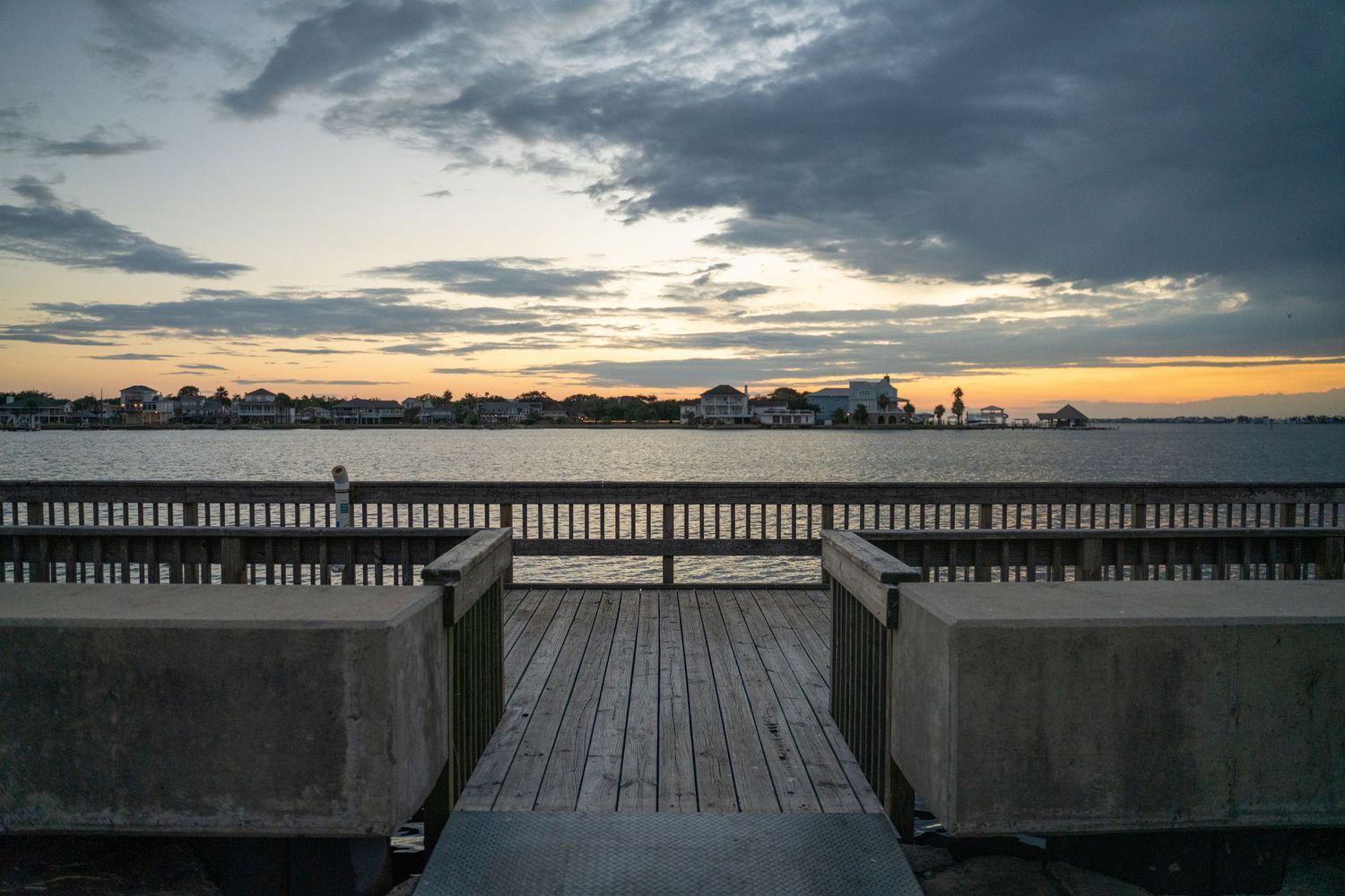 Panoramic sunset view over a wooden pier with dramatic cloudy sky and ocean horizon.
