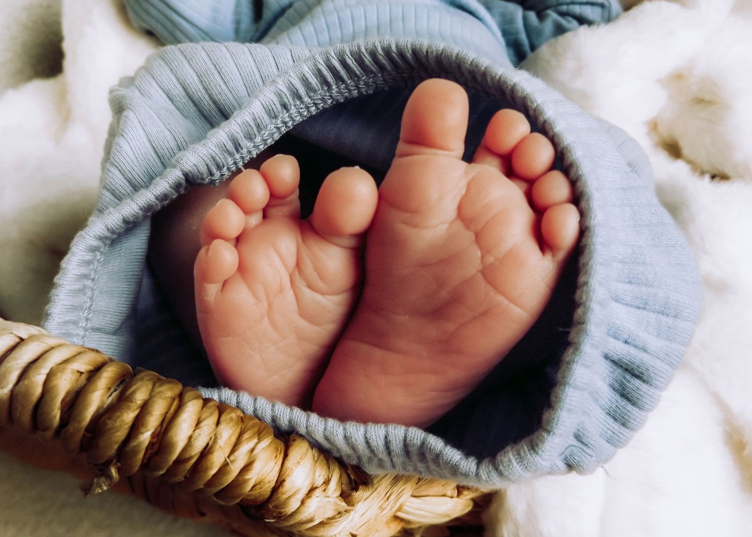 Close-up of tiny newborn baby feet peeking out from under a blue blanket.