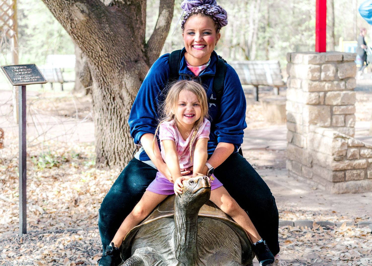 Family enjoying outdoor activities at a nature park with trees and stone structures.