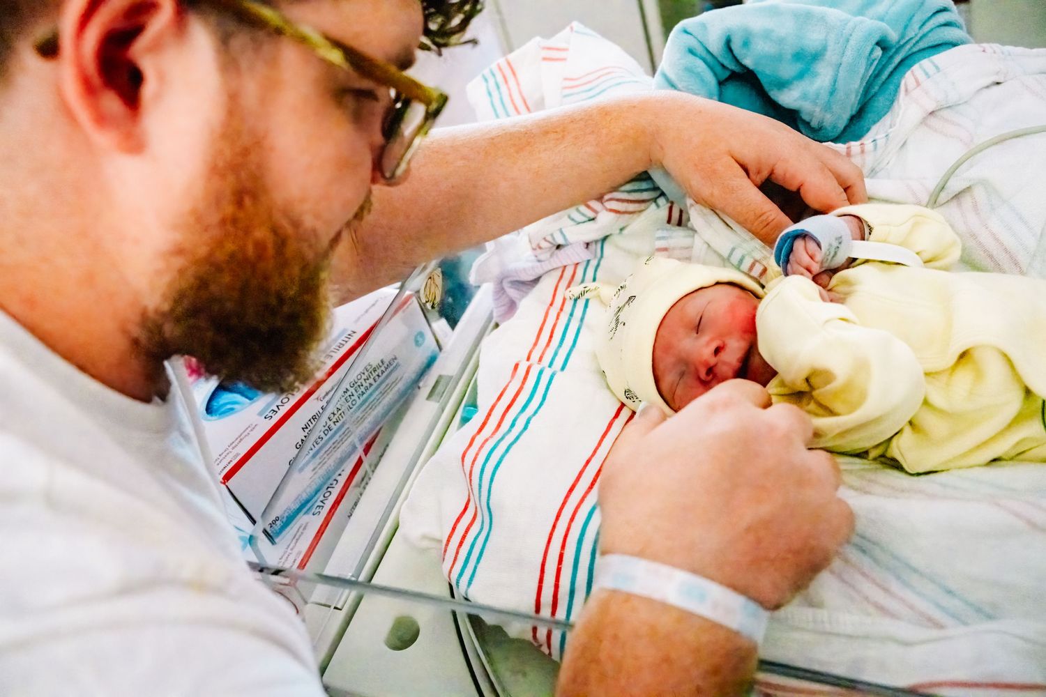A tender moment as a parent tends to their newborn baby swaddled in striped blankets.