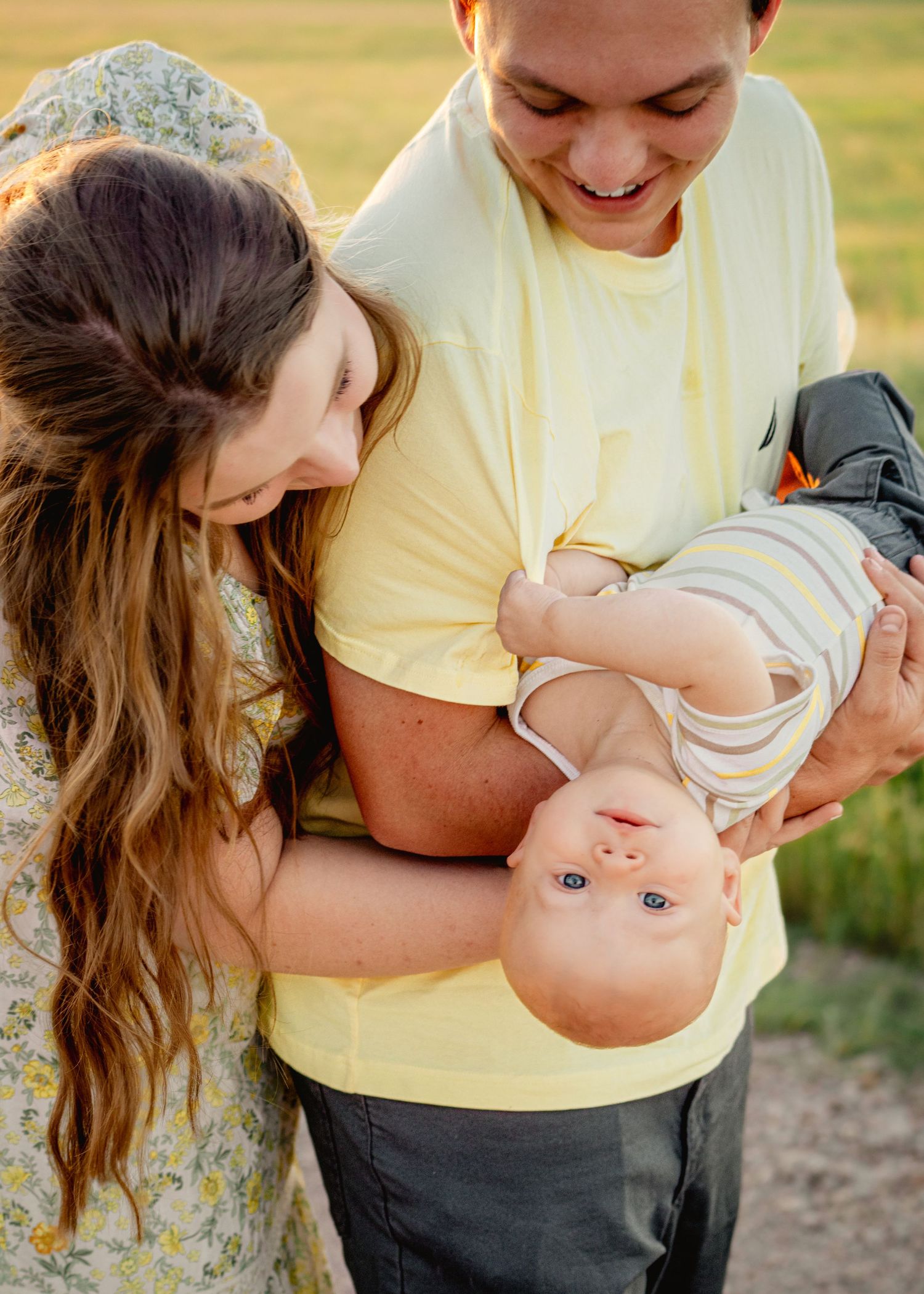 A family plays with their baby during a casual outdoor photo session in warm sunlight.