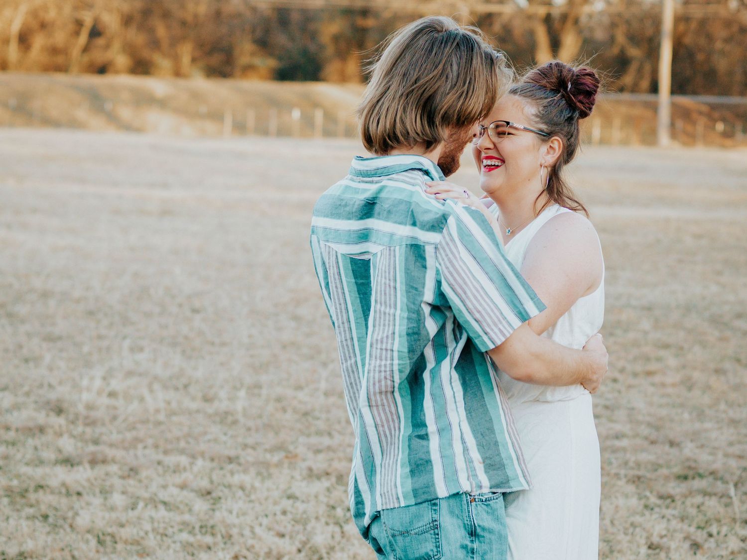Couple laughing together outdoors wearing turquoise striped shirt and white dress.