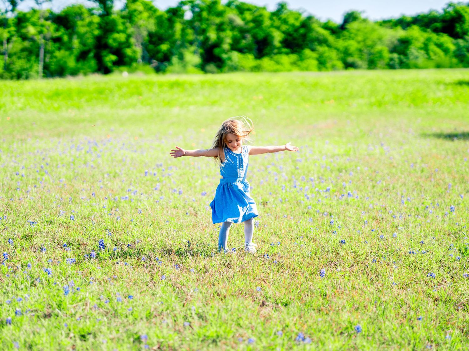 Person in blue dress twirling joyfully in a sunny green meadow.