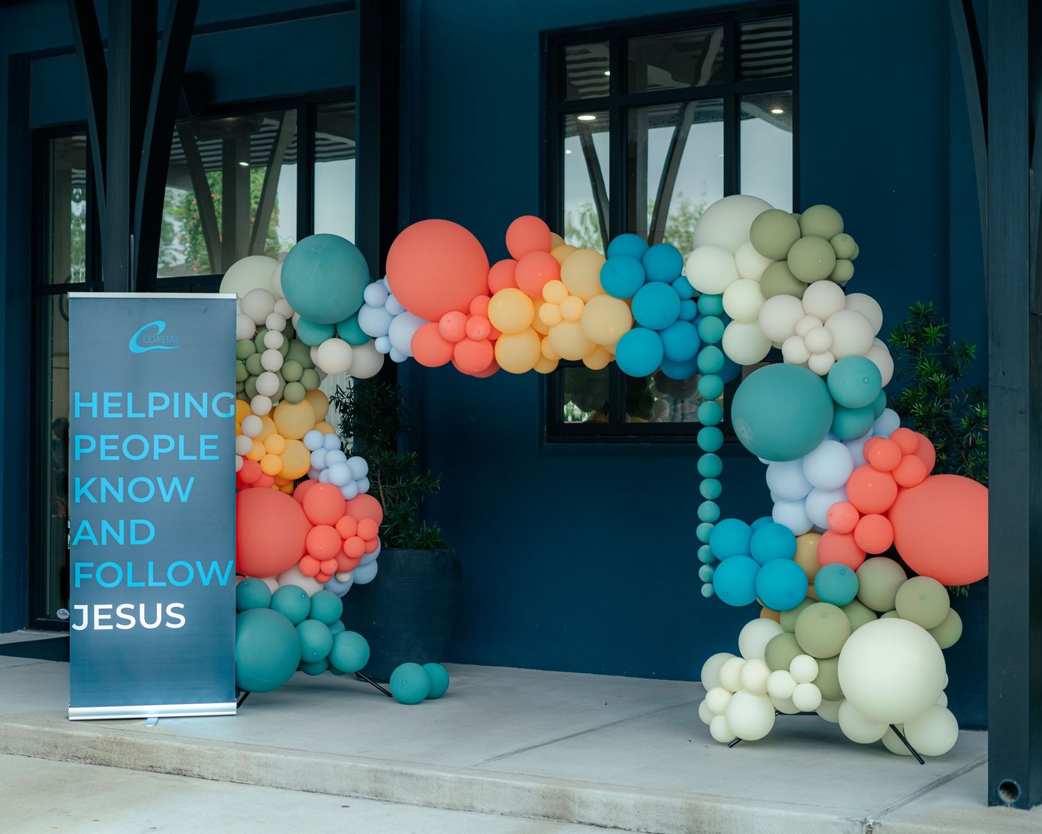 Colorful balloon arches in coral, teal and cream decorate a modern church entrance.