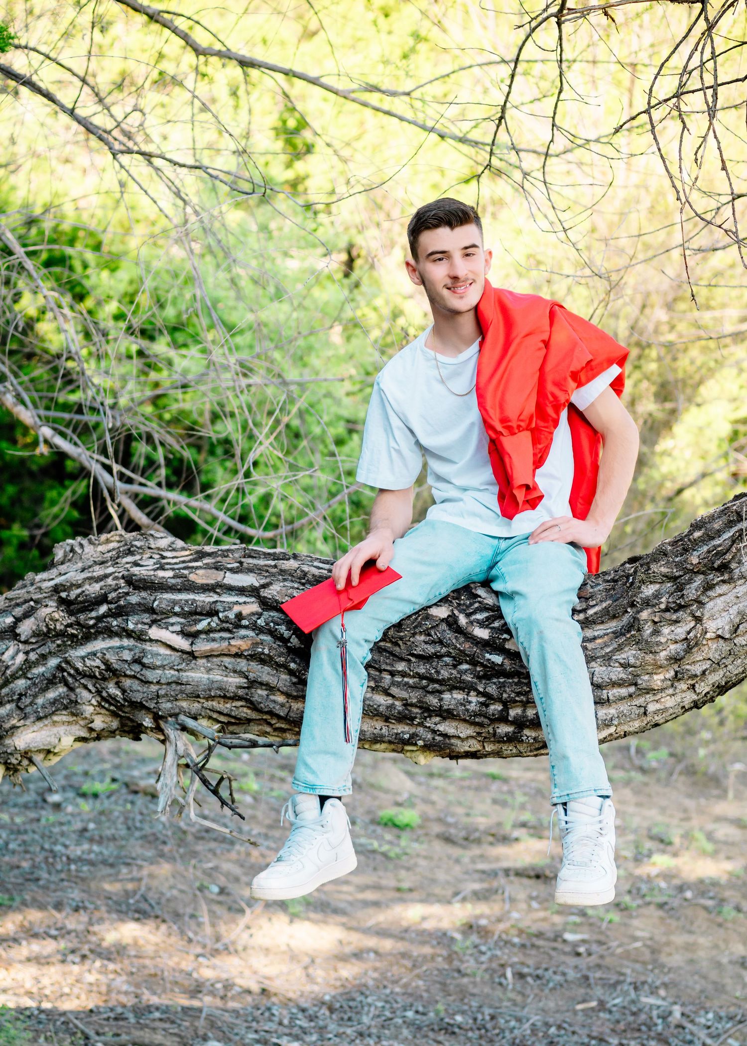 Person in light blue jeans and red top sitting casually on a fallen tree trunk in a natural outdoor setting.