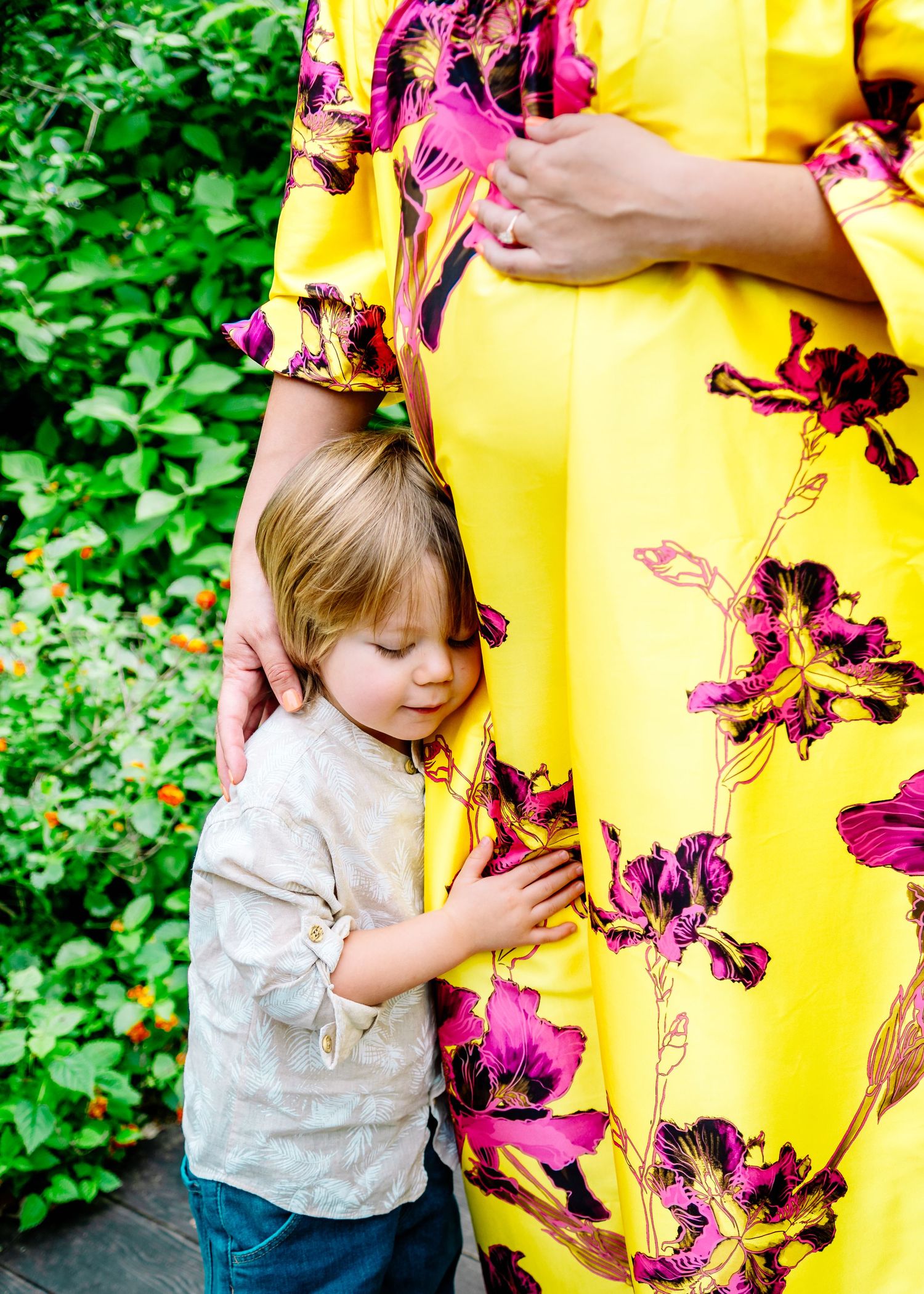 Sweet moment captured as small child hugs yellow floral dress in garden setting.