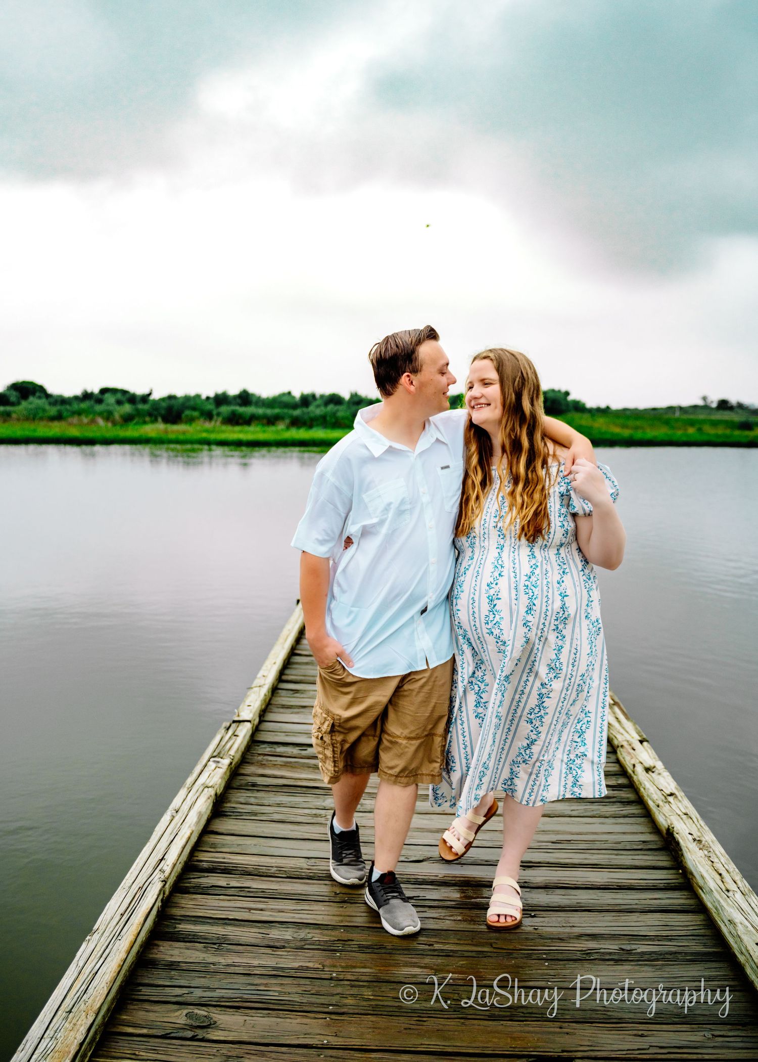 Couple shares romantic moments together on a wooden dock overlooking a serene lake.