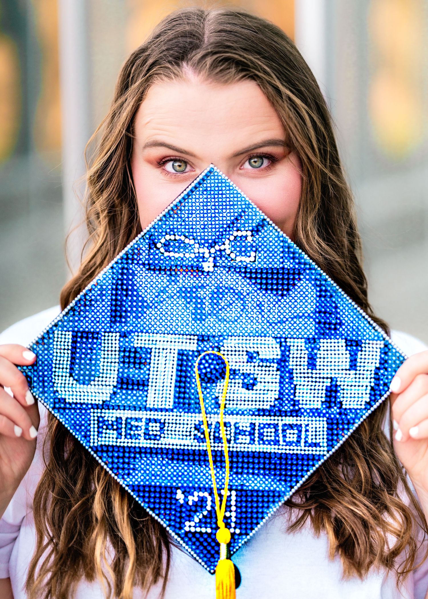 Decorated graduation cap with blue sparkly UTEP design held up in portrait style photo.