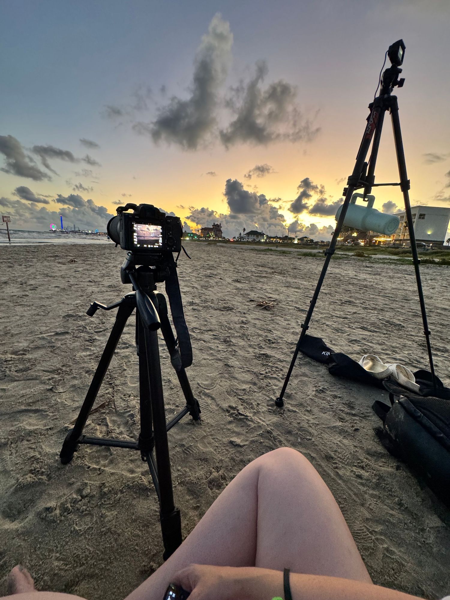 Camera equipment set up on beach during golden hour with tripods in silhouette.