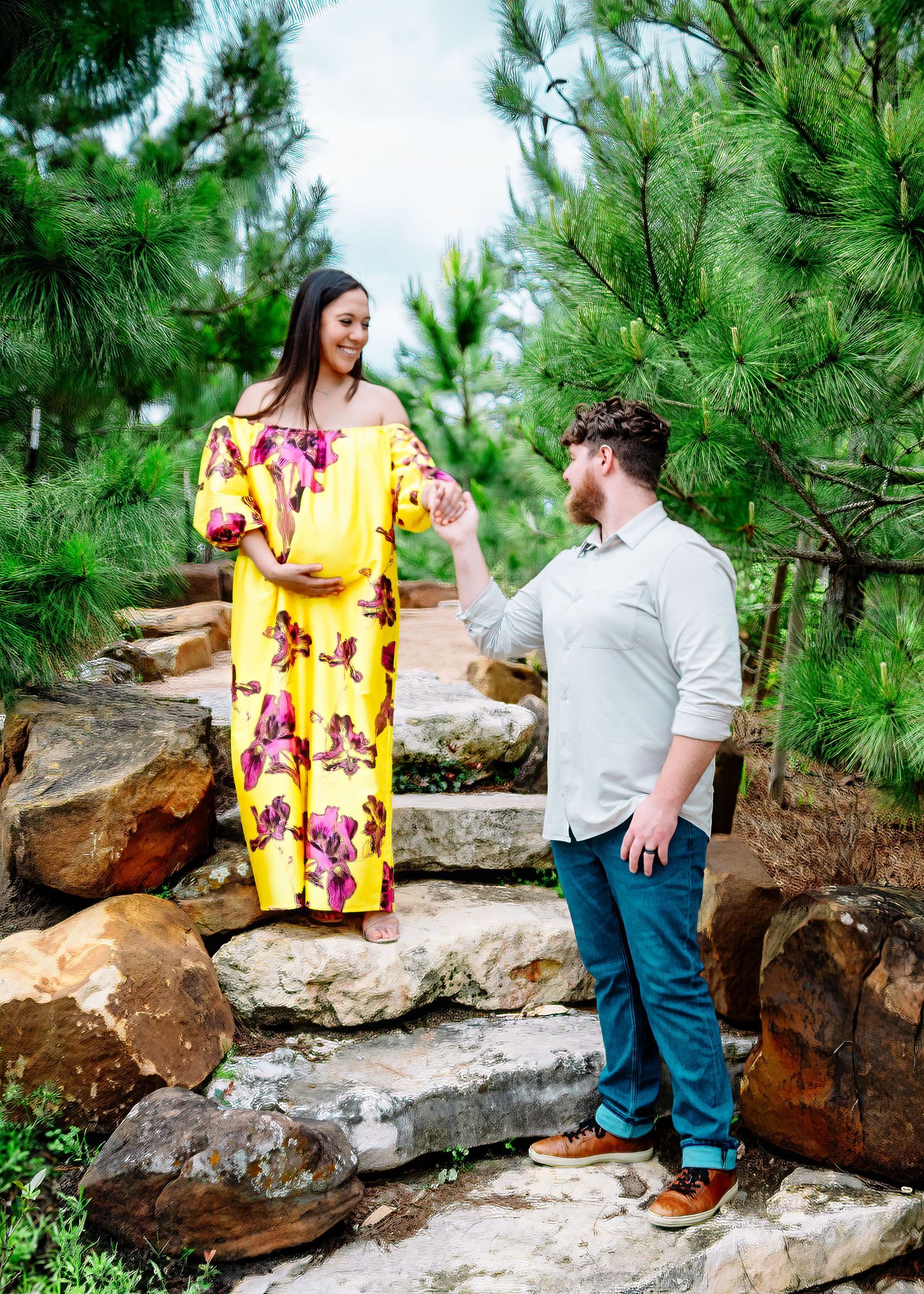 A couple shares a joyful moment on rocky steps surrounded by tall pine trees.