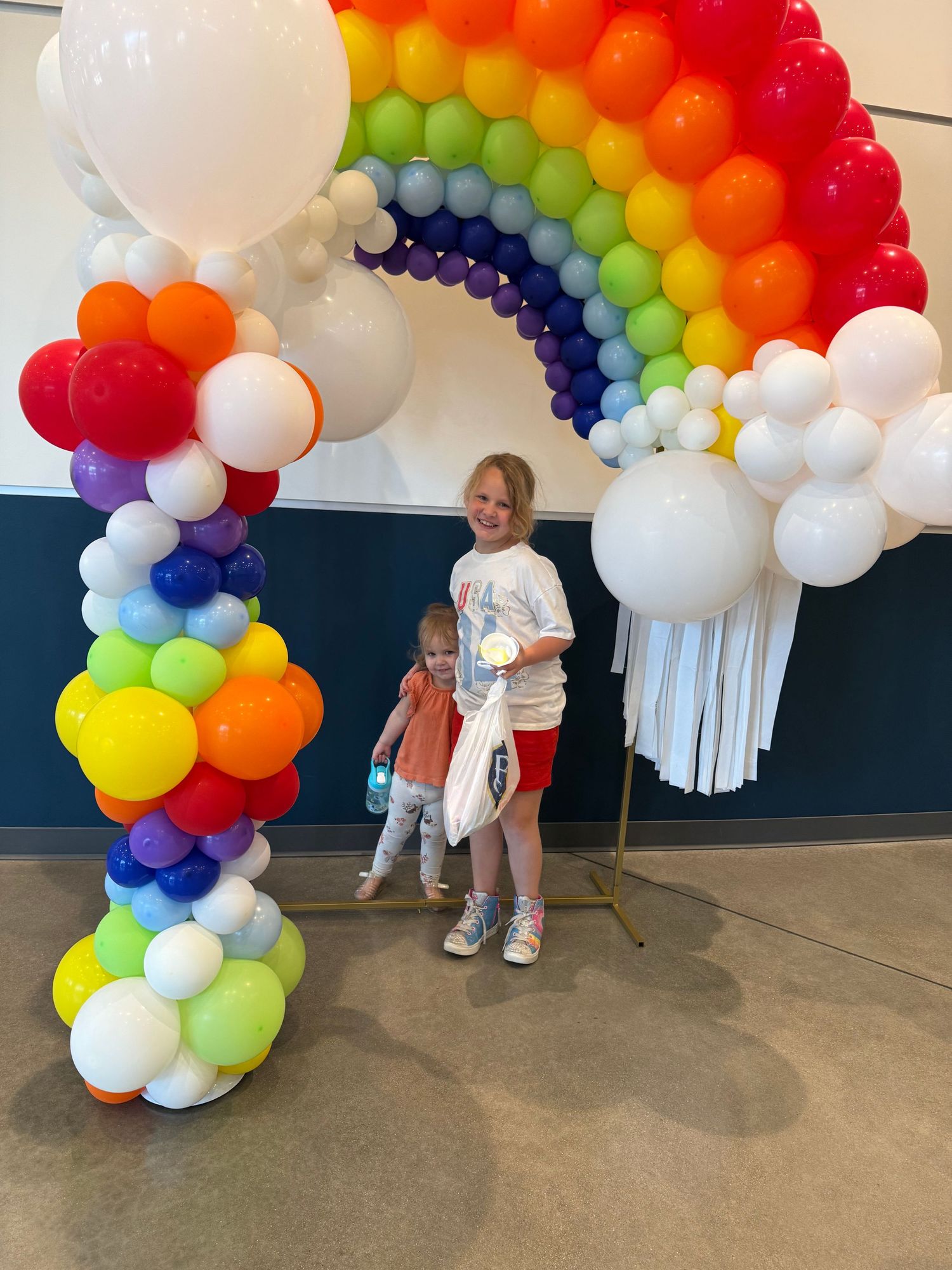 Colorful rainbow balloon arch display with white cloud-like balloons creating a festive party atmosphere.