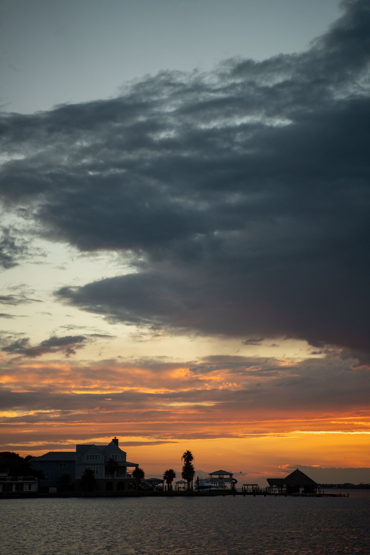 Dramatic sunset silhouettes coastal homes against an orange and purple sky.
