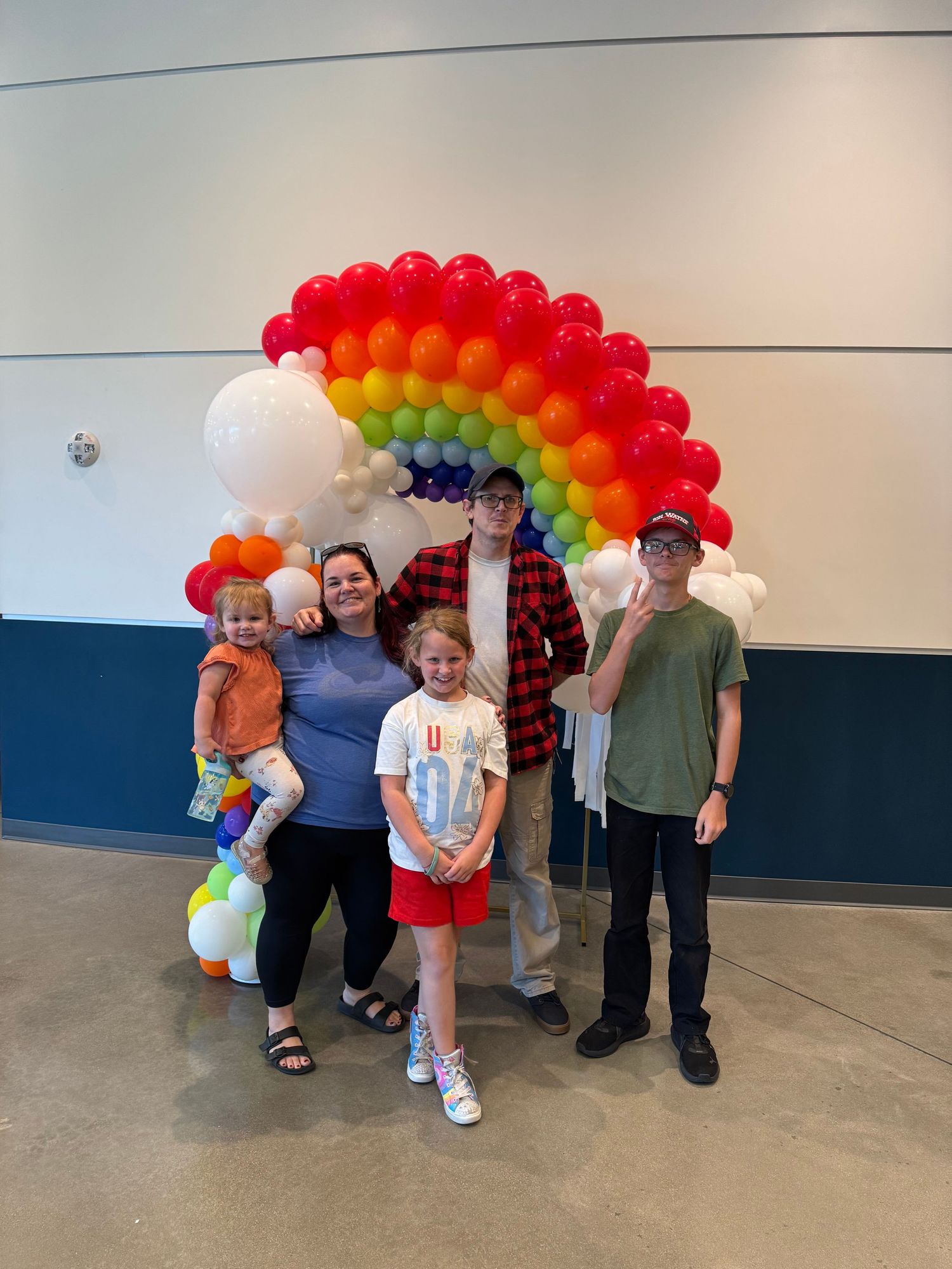 Rainbow balloon arch display with white accents in an indoor venue setting.