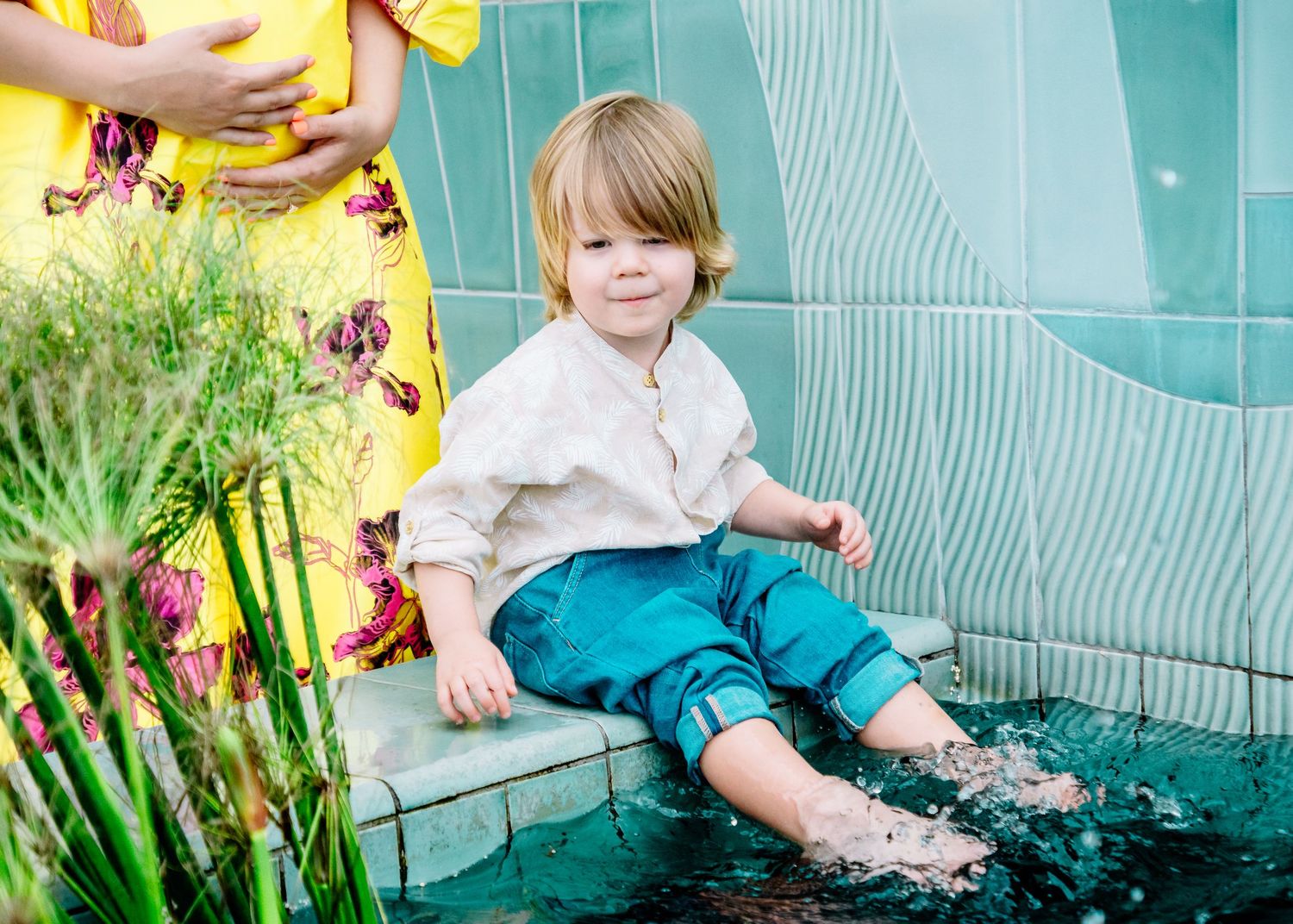 A toddler plays near a turquoise wall wearing casual clothing in an outdoor setting.