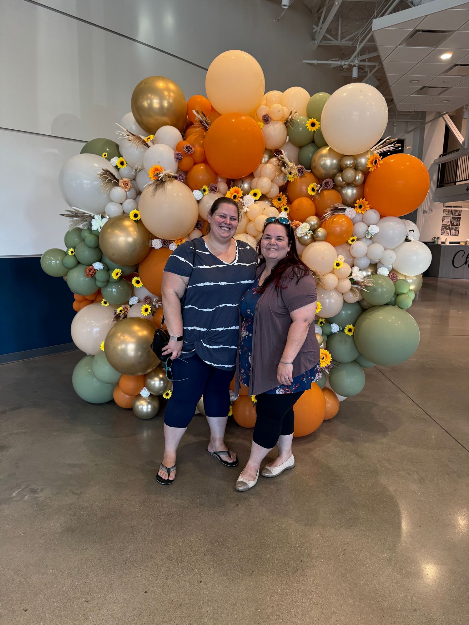 Couple standing in front of a decorative balloon wall with orange, gold and sage green spheres.