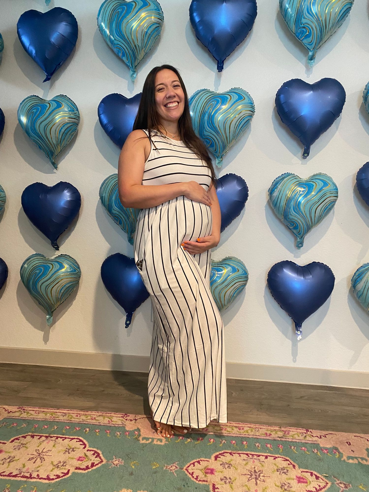 Maternity photo with blue and turquoise heart balloons decorating white wall background.