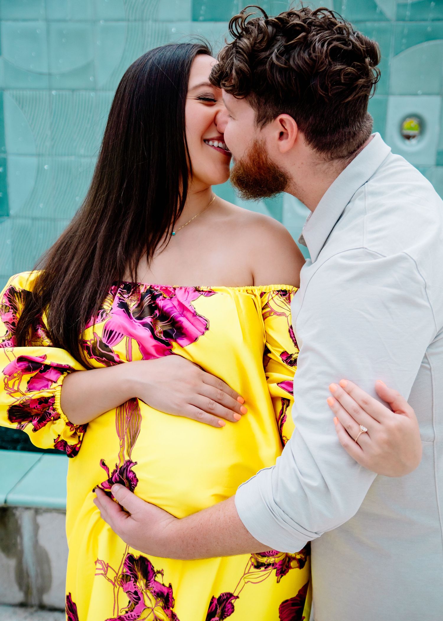 Romantic couple embraces tenderly against turquoise wall backdrop.