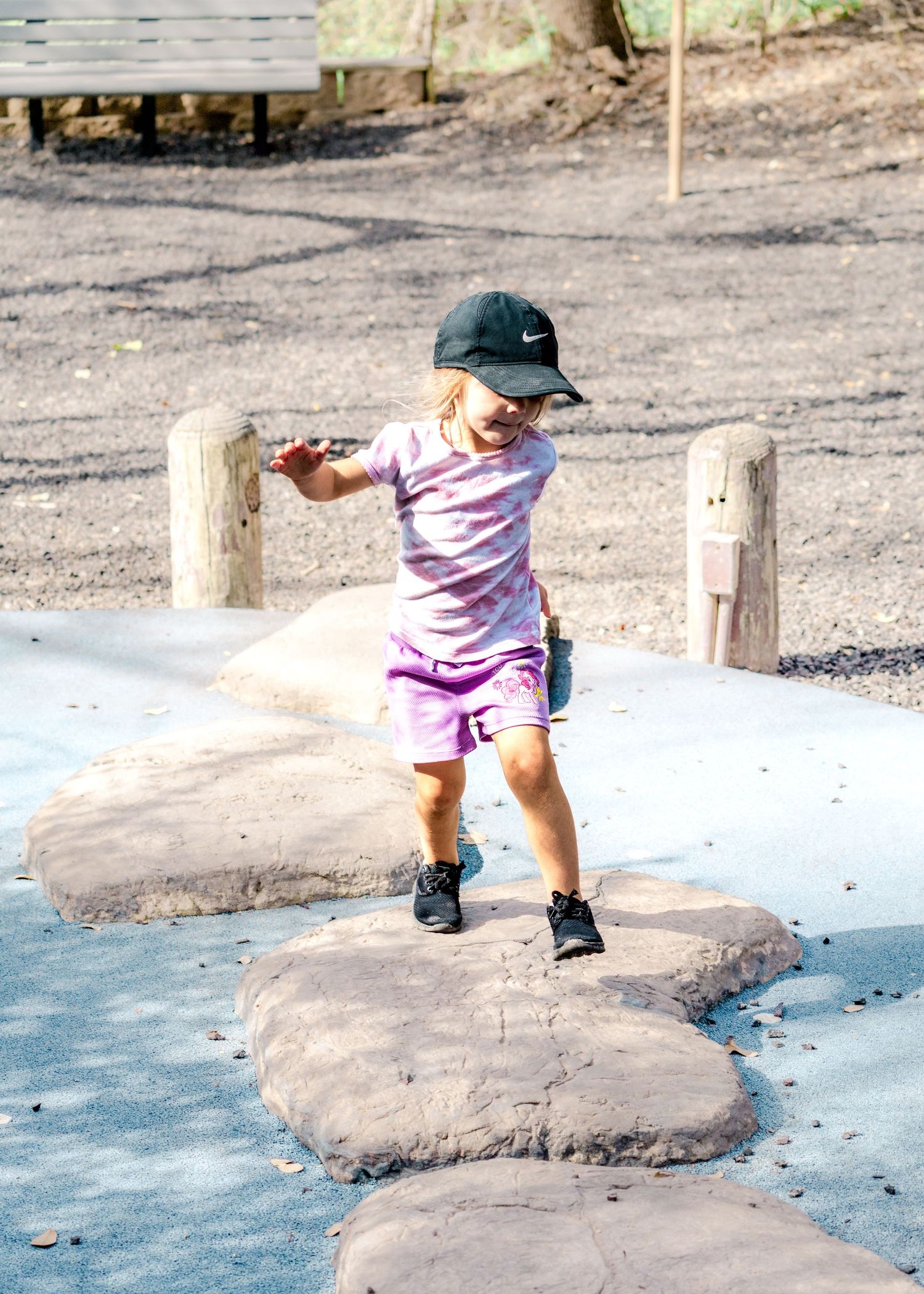 Child jumping between stepping stones on a blue playground surface.