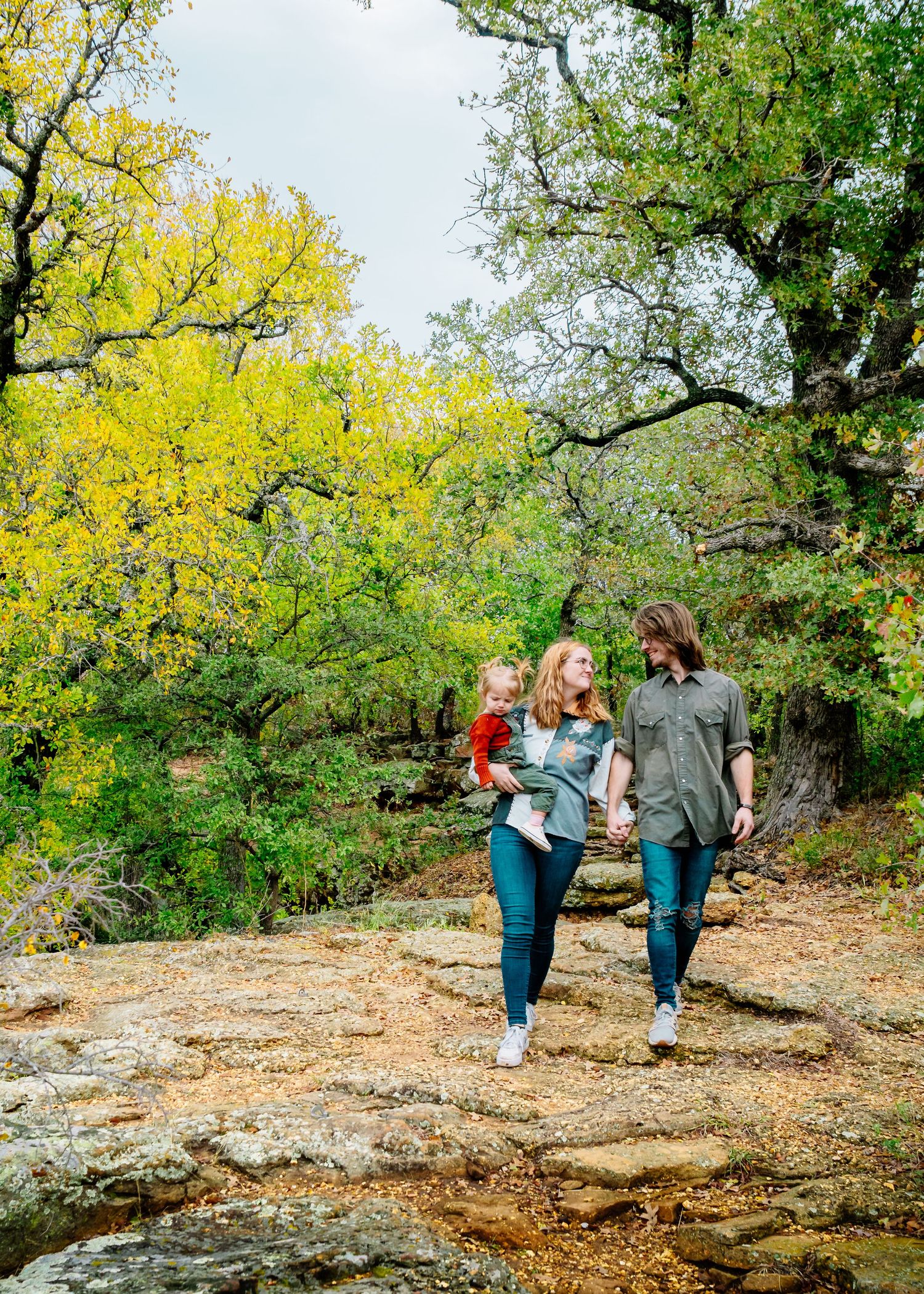 Two figures walking along a rocky path with yellow flowering trees in the background.